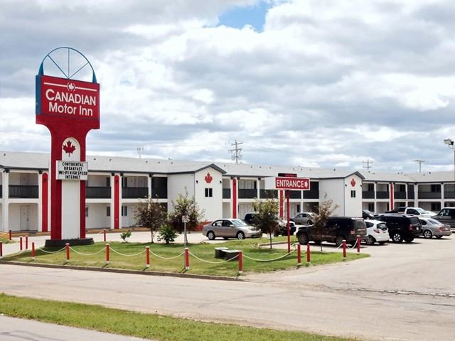 Exterior of Canadian Motor Inn with parked cars and maple leaf signage.