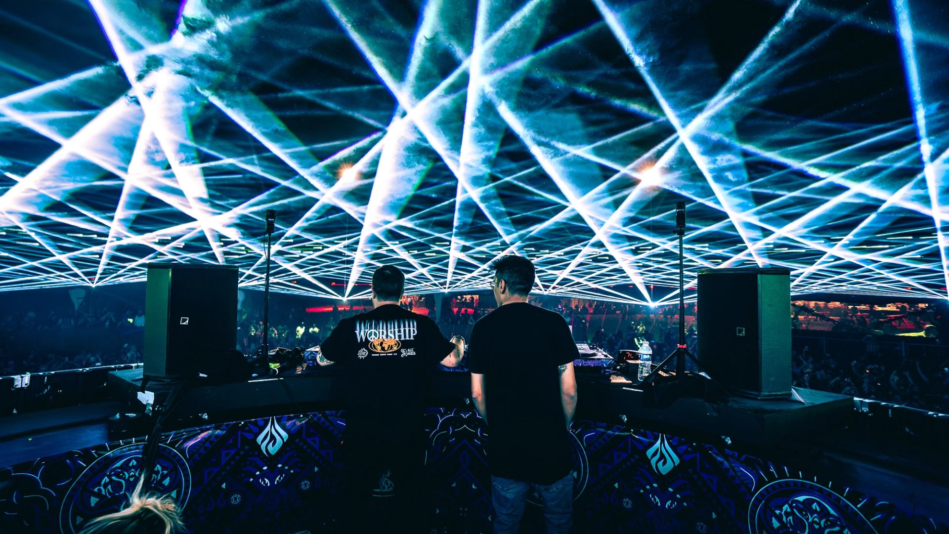DJs take center stage under a mesmerizing canopy of lasers and lights, electrifying the crowd at a packed music festival.