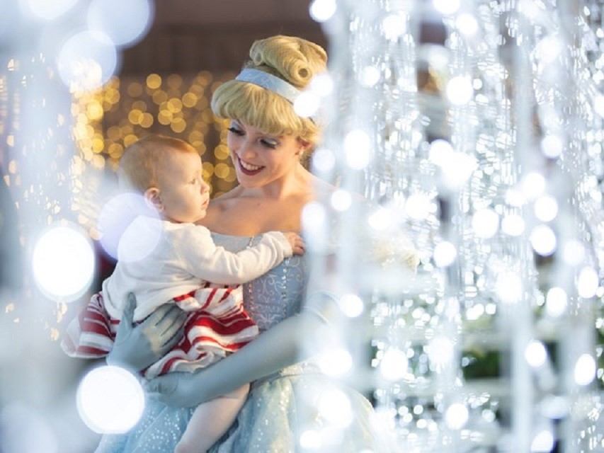 Person holding a baby surrounded by sparkling holiday lights at Glow Christmas Festival.