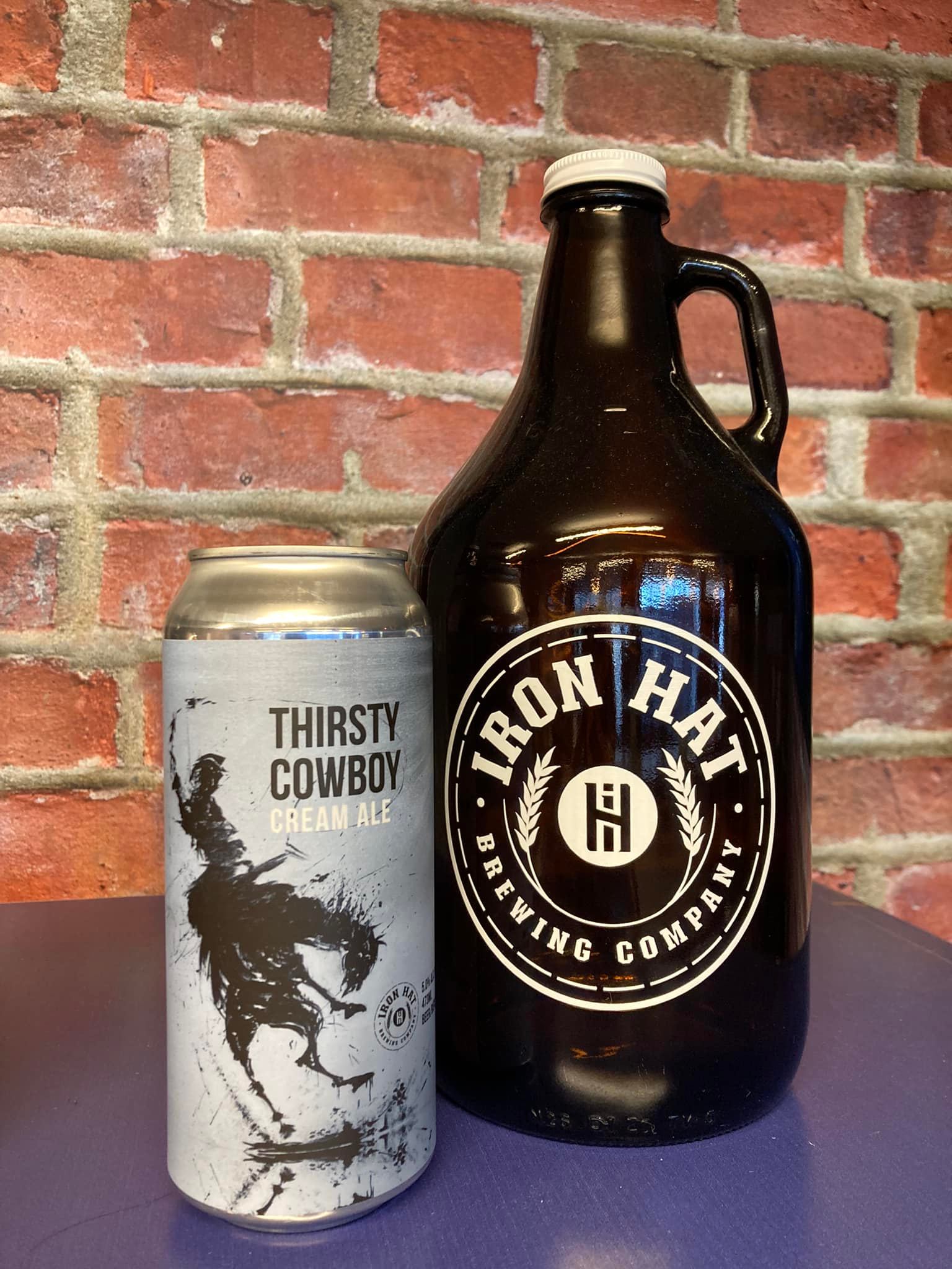 Beer can and growler from Iron Hat Brewing Company against a brick wall.
