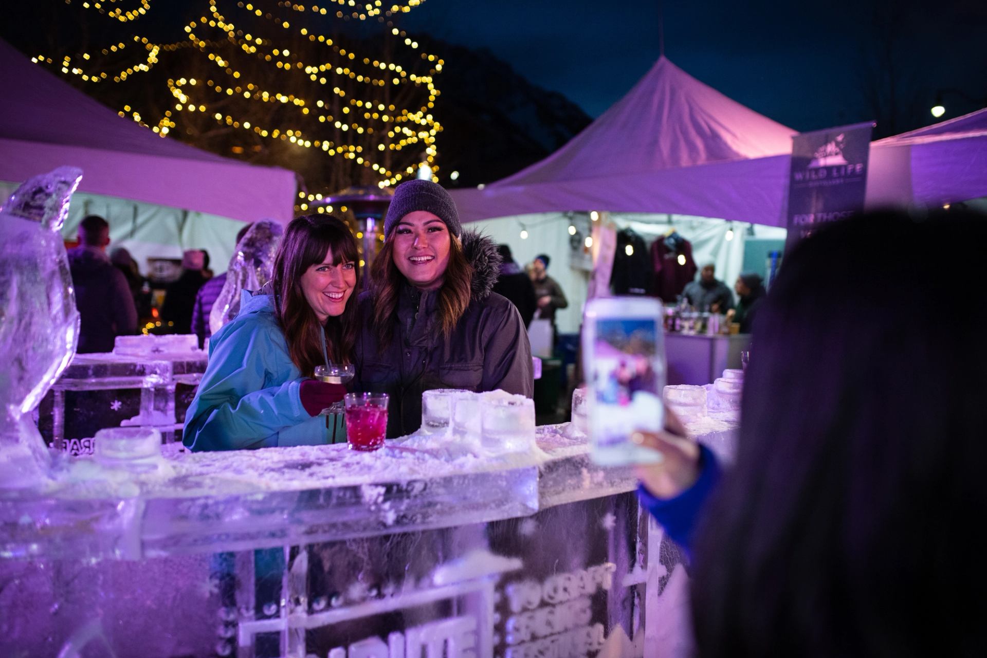 Guests posing with drinks at an ice bar under string lights at Tribute to Craft.