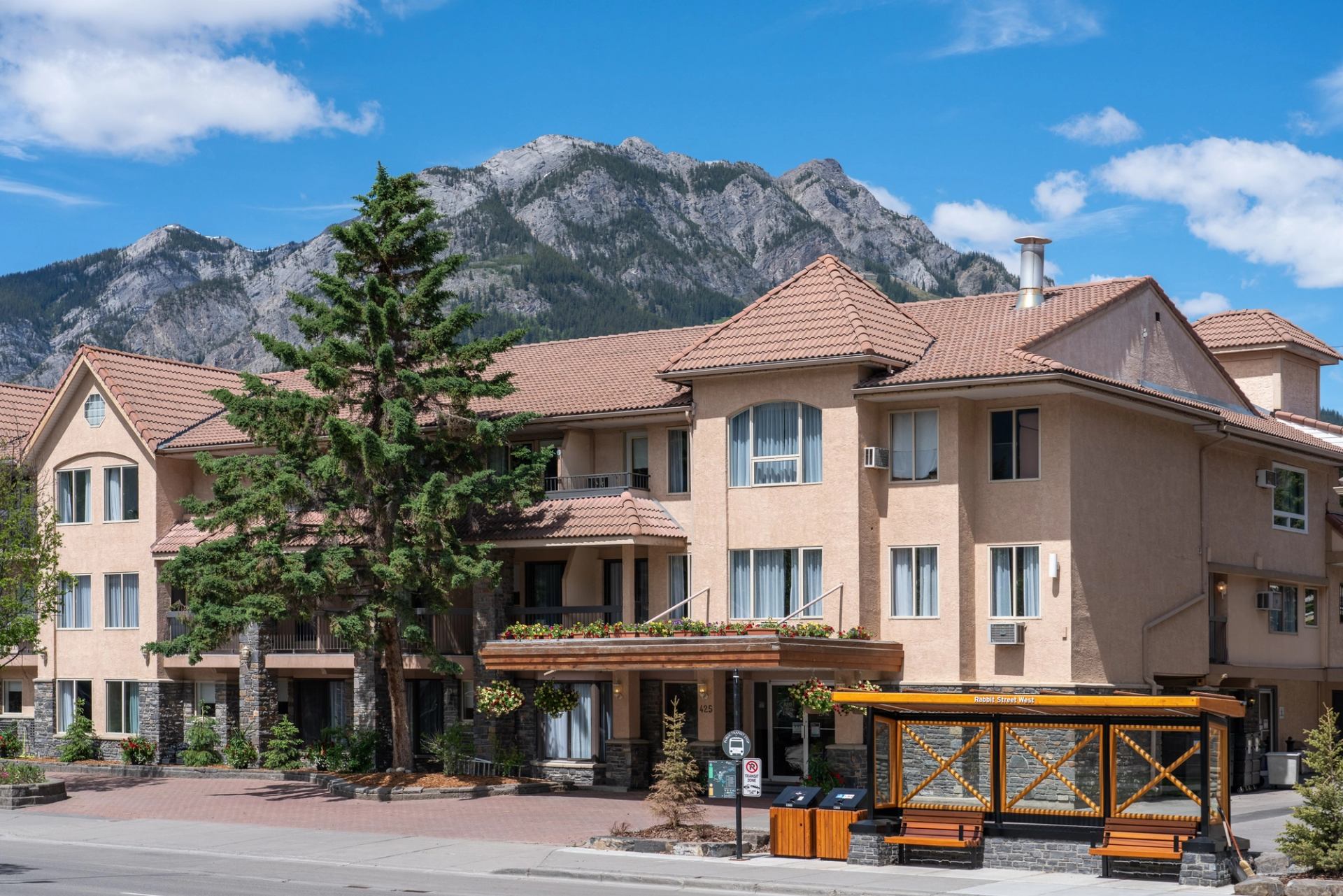 Hotel exterior with balconies, mountain backdrop, and bright blue sky.
