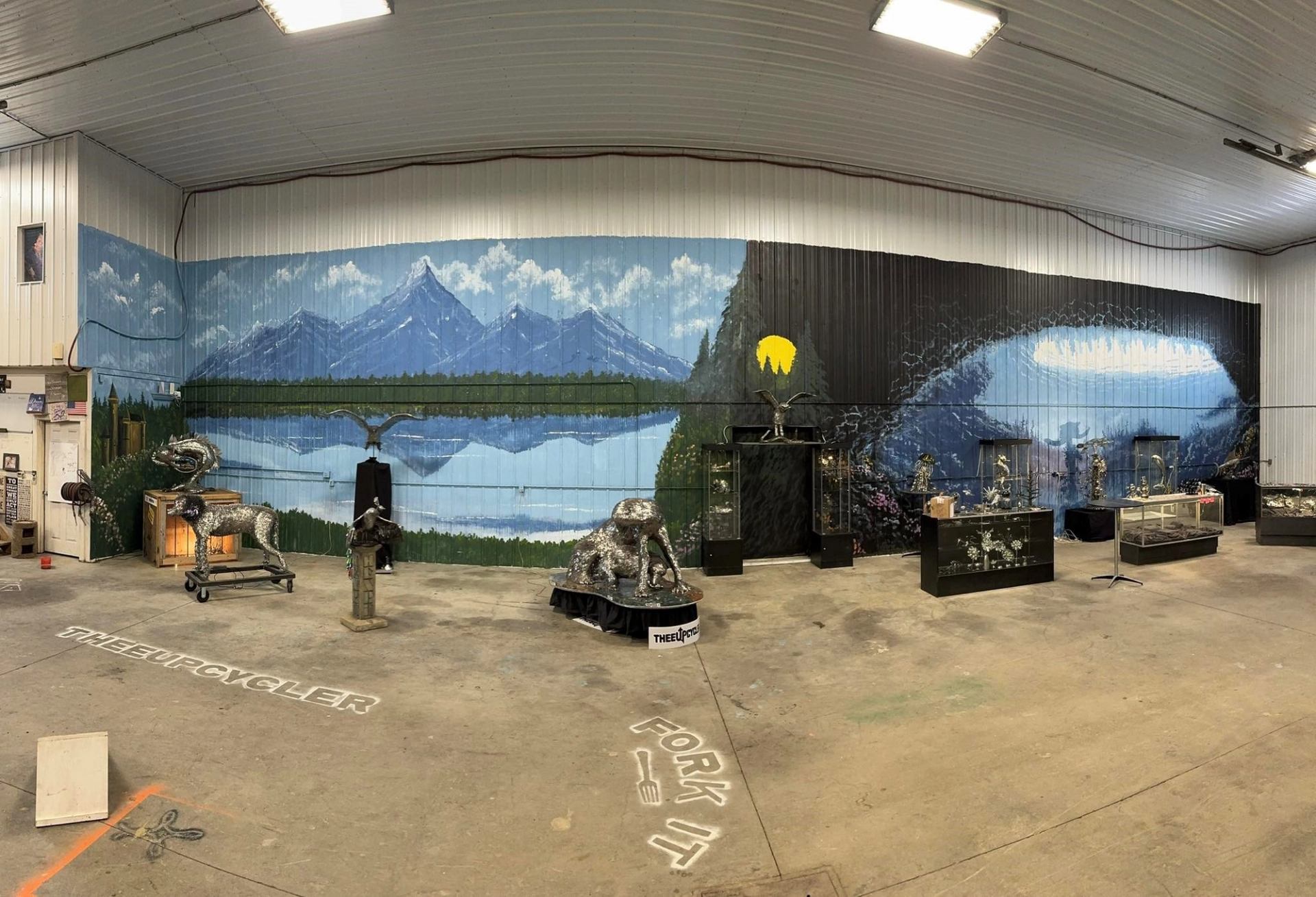 Gallery interior with mountain mural, metal animal sculptures and display cases.