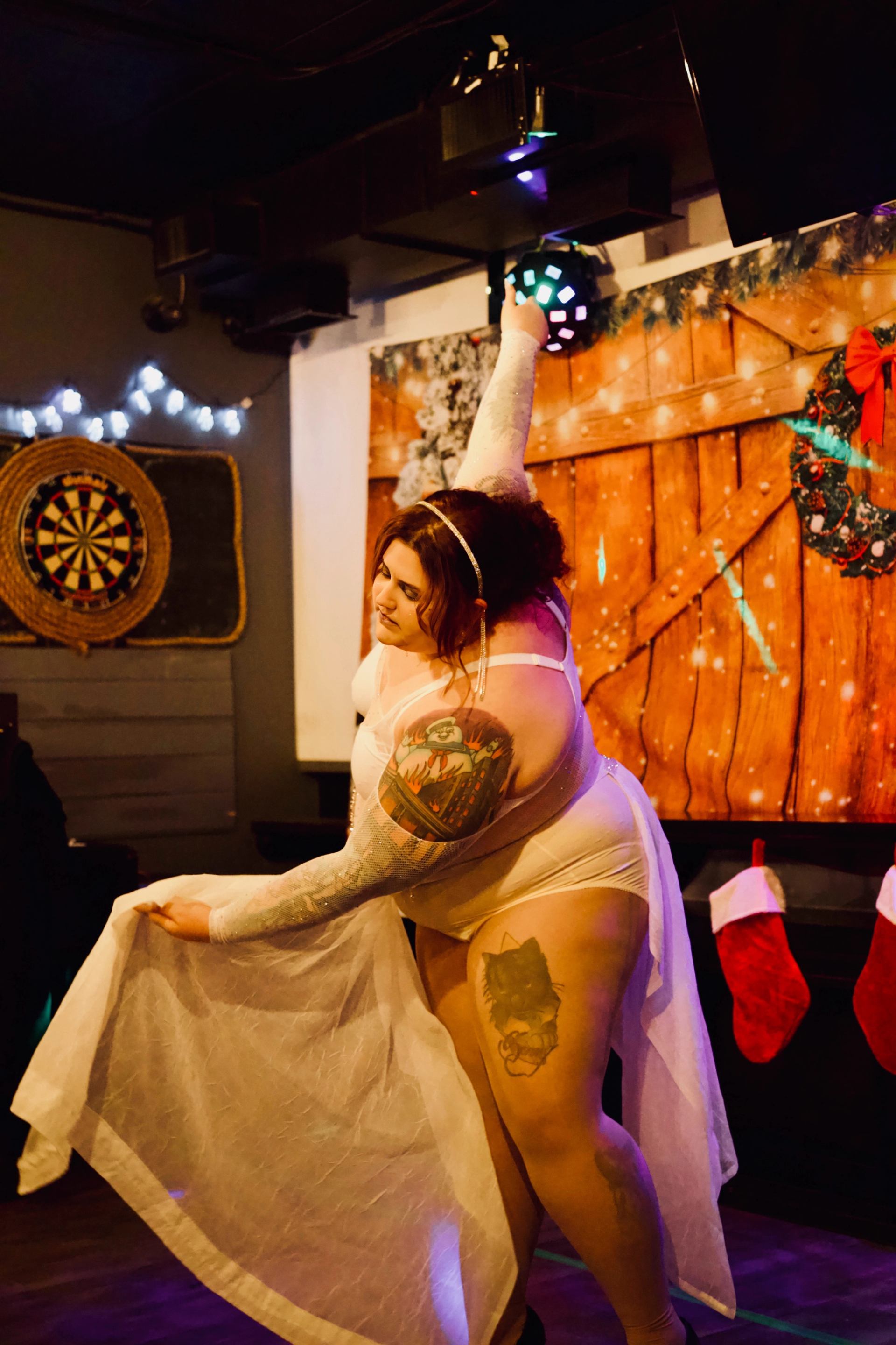 Performer in white costume on decorated stage with stockings and lights.