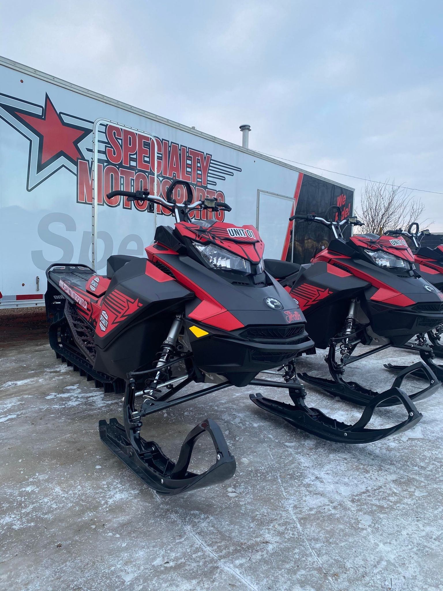 Red and black snowmobiles parked outside Specialty Motorsports Ltd building sign.