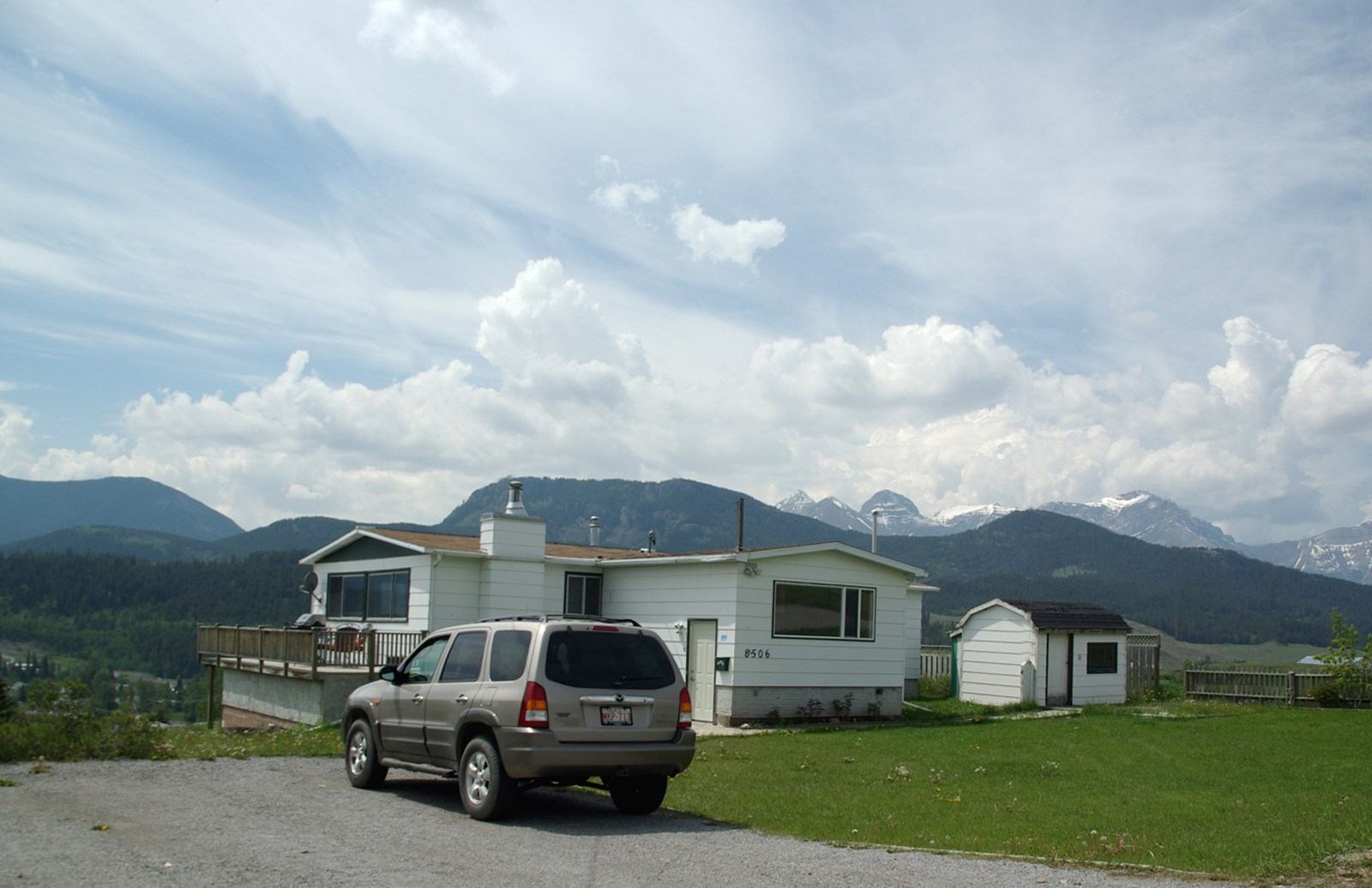 White vacation home with deck, parked SUV, and mountains in background