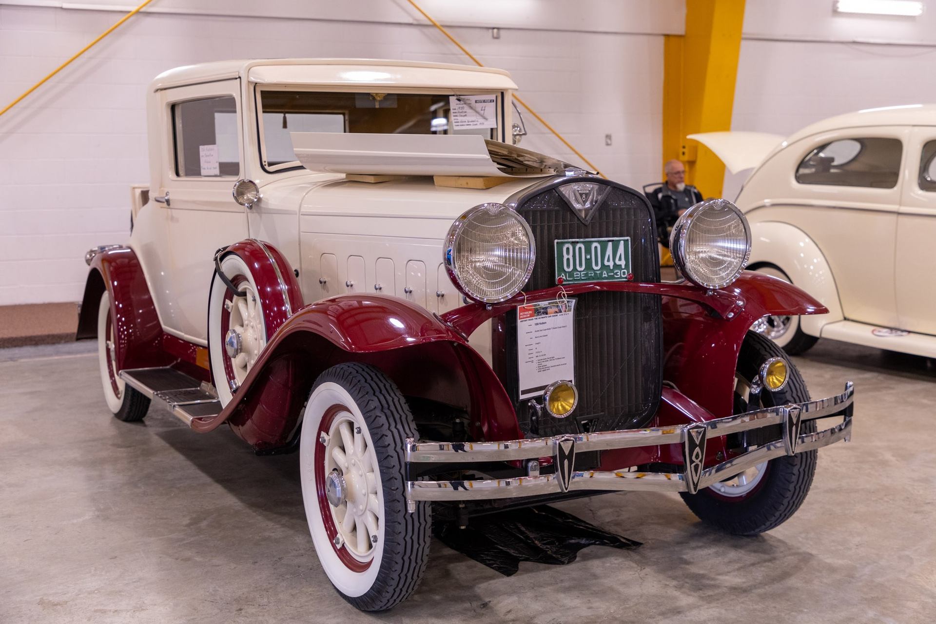 A cream and maroon vintage car with large headlights and running boards on display.