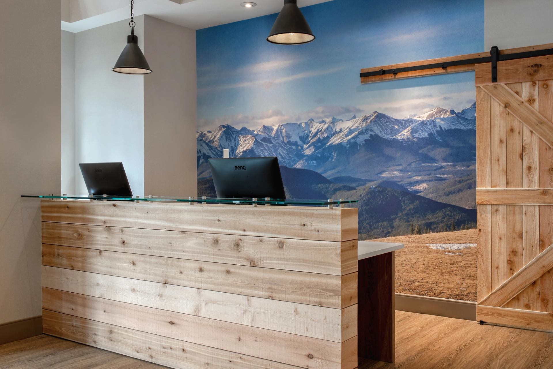 Reception desk with wood panelling, computers and mountain landscape mural behind.