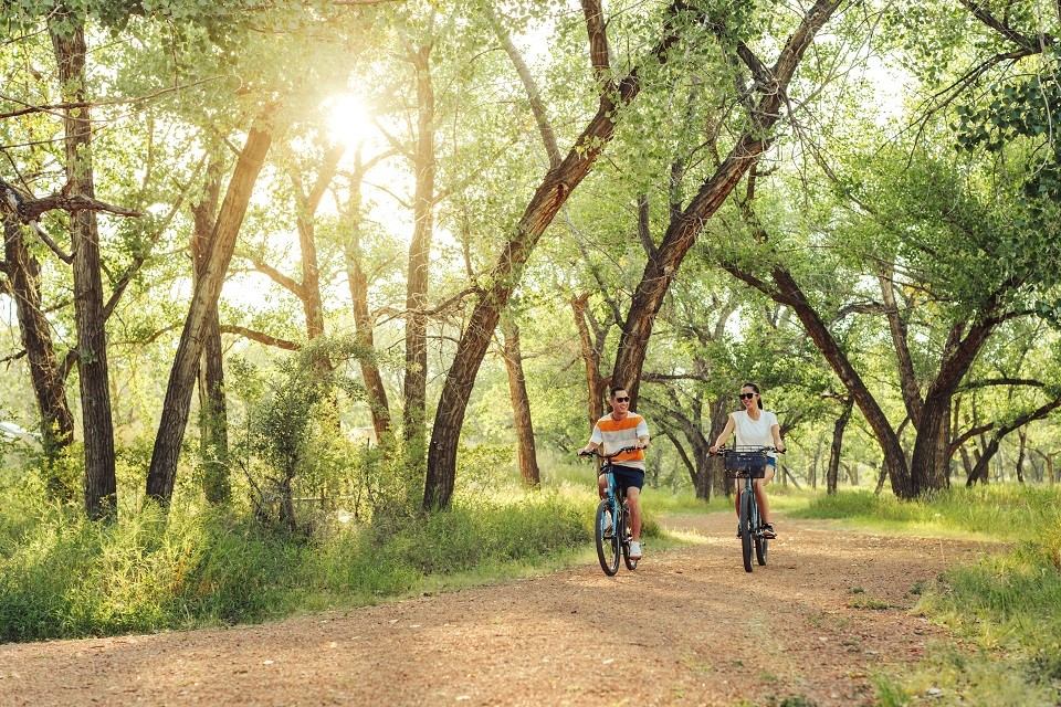 Two people biking on a forest path at Strathcona Island Park with sunlight filtering through trees.