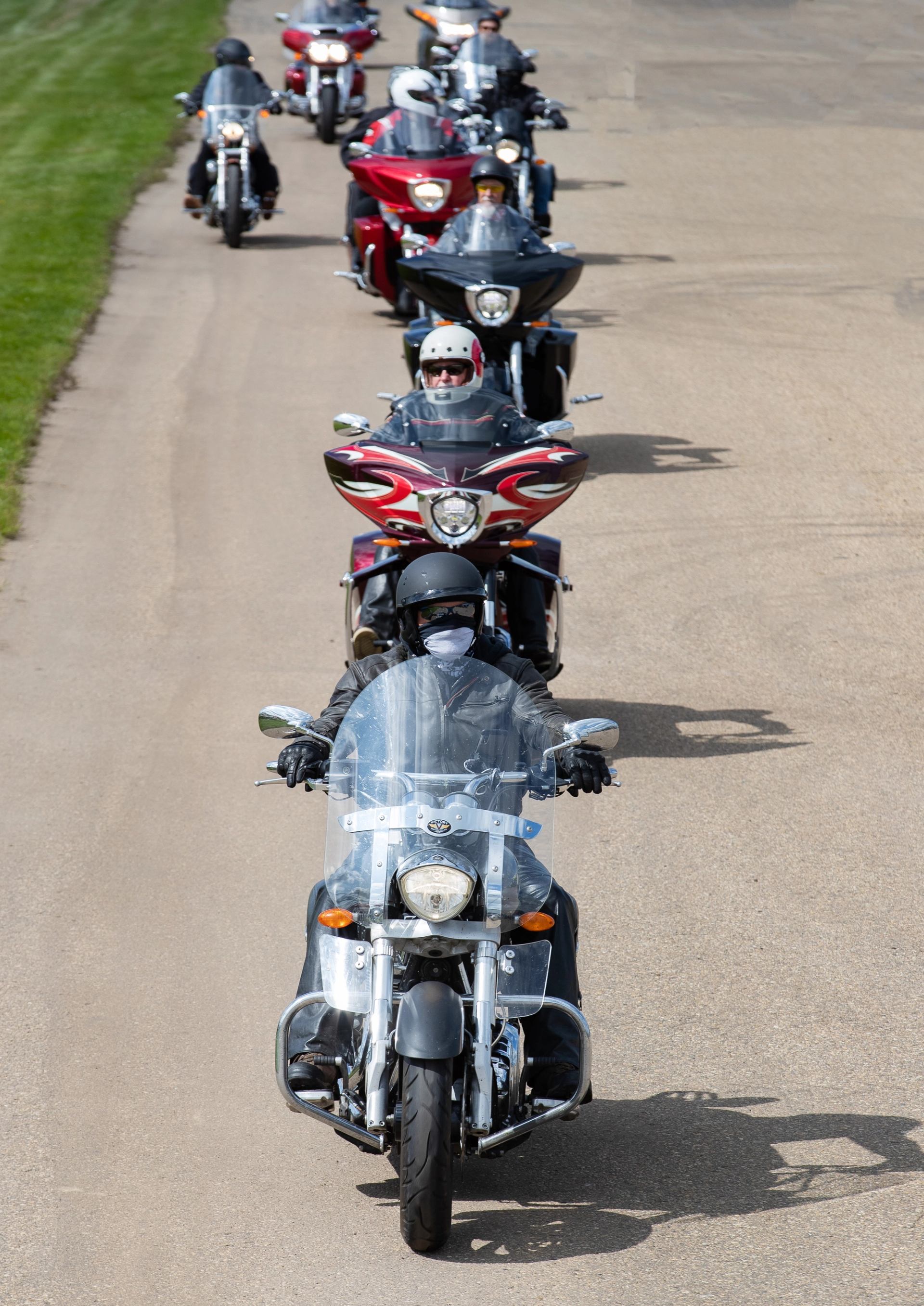 Motorcyclists ride in a line down a road, close-up of front bikes and helmets.