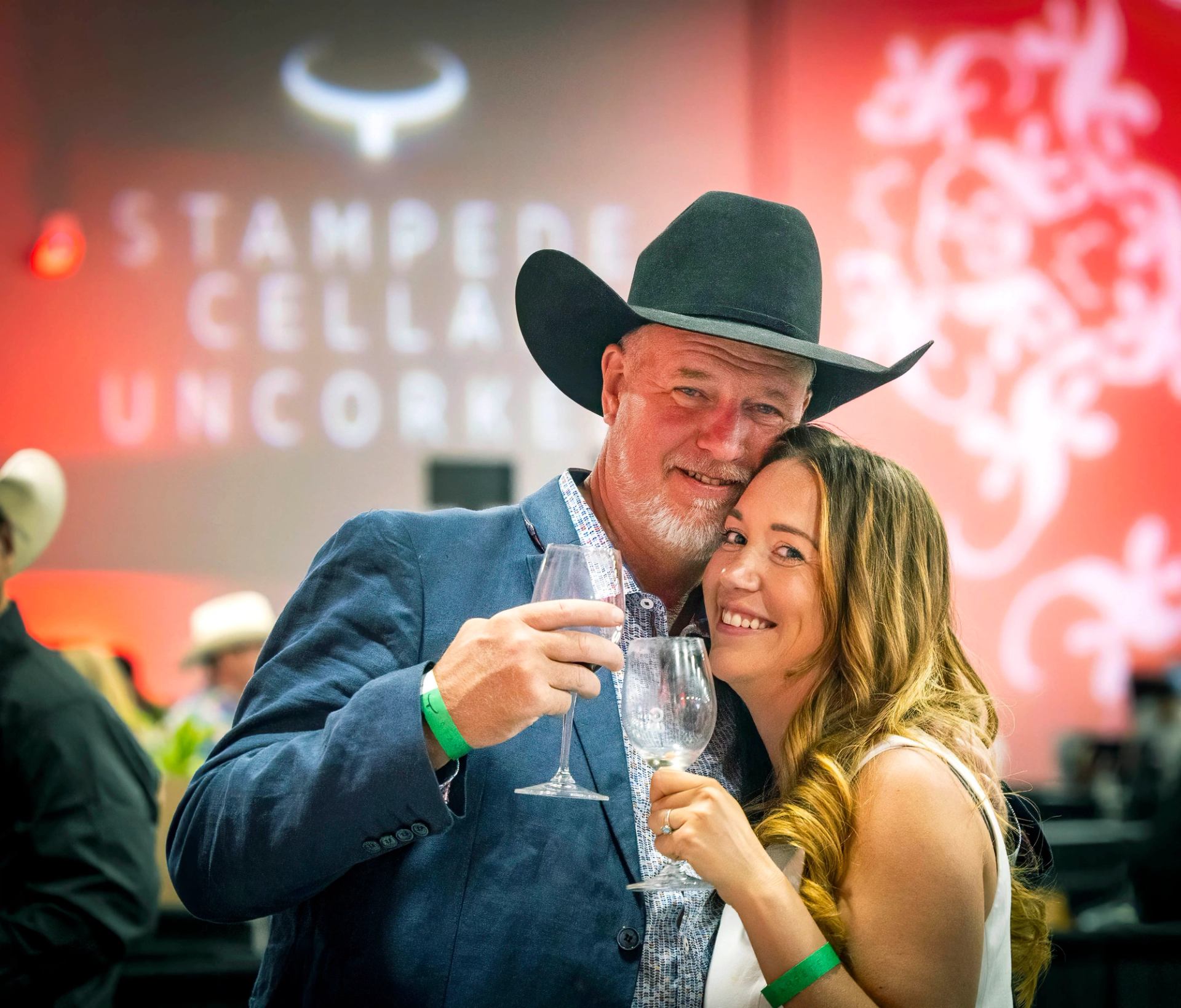 Two guests holding wine glasses with the event backdrop behind them