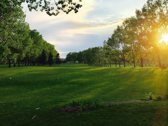 Golf course fairway with trees and distant hills under a partly cloudy sky.