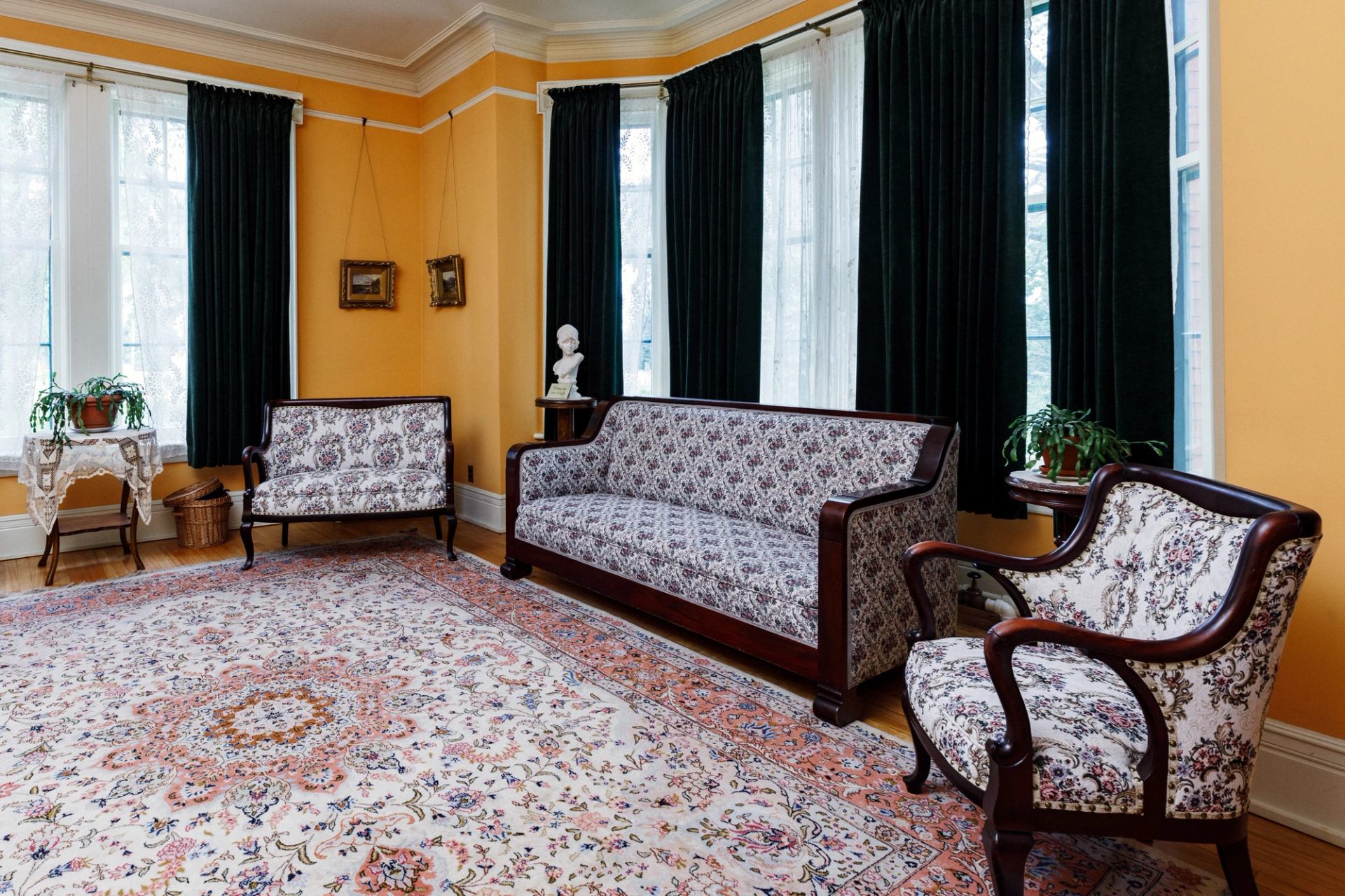 Historic room with upholstered sofa, armchair, floral curtains, and framed pictures.