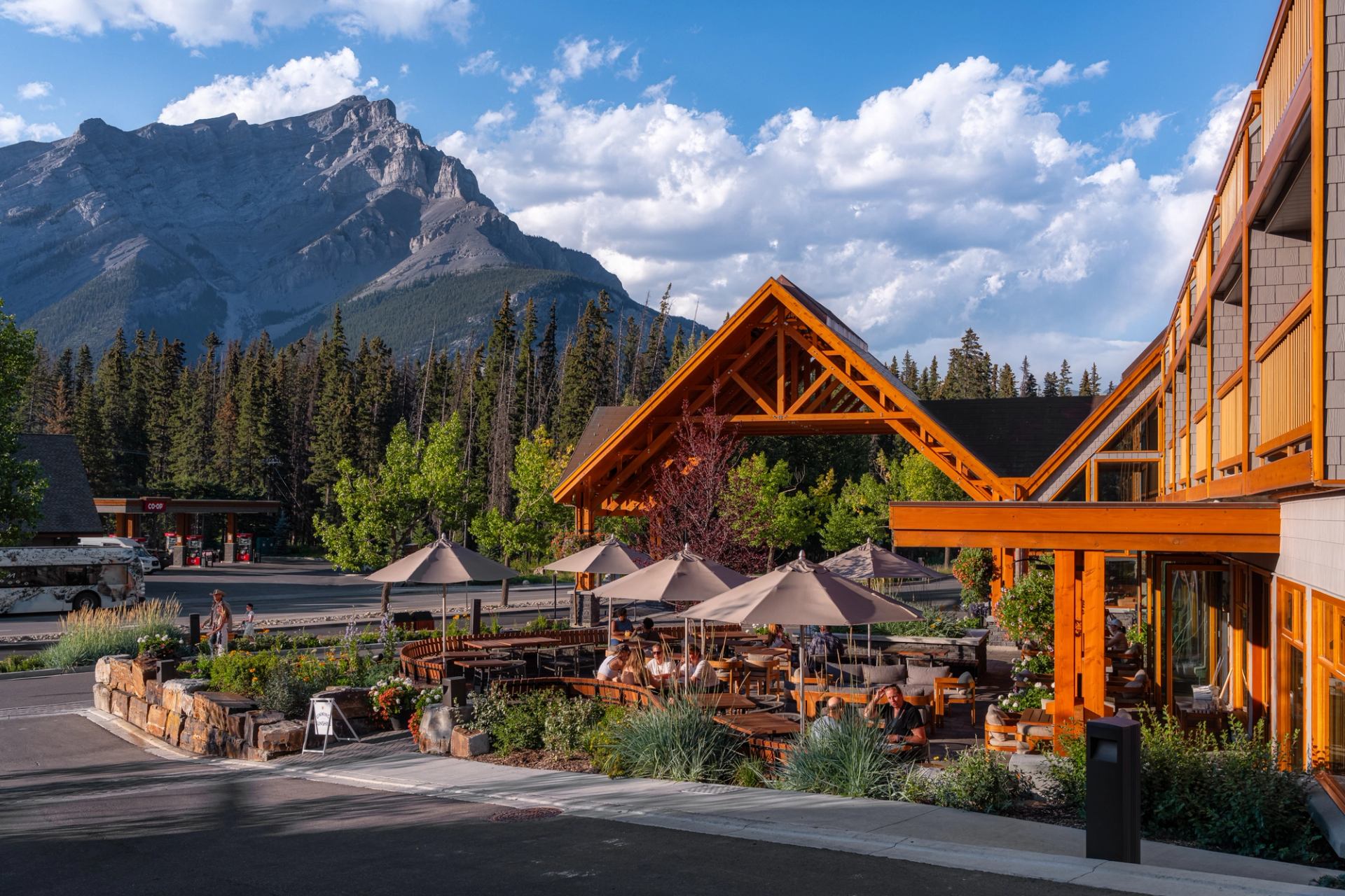 Patio with grey umbrellas, building with wood beams and a mountain in the back with cloudy blue sky.