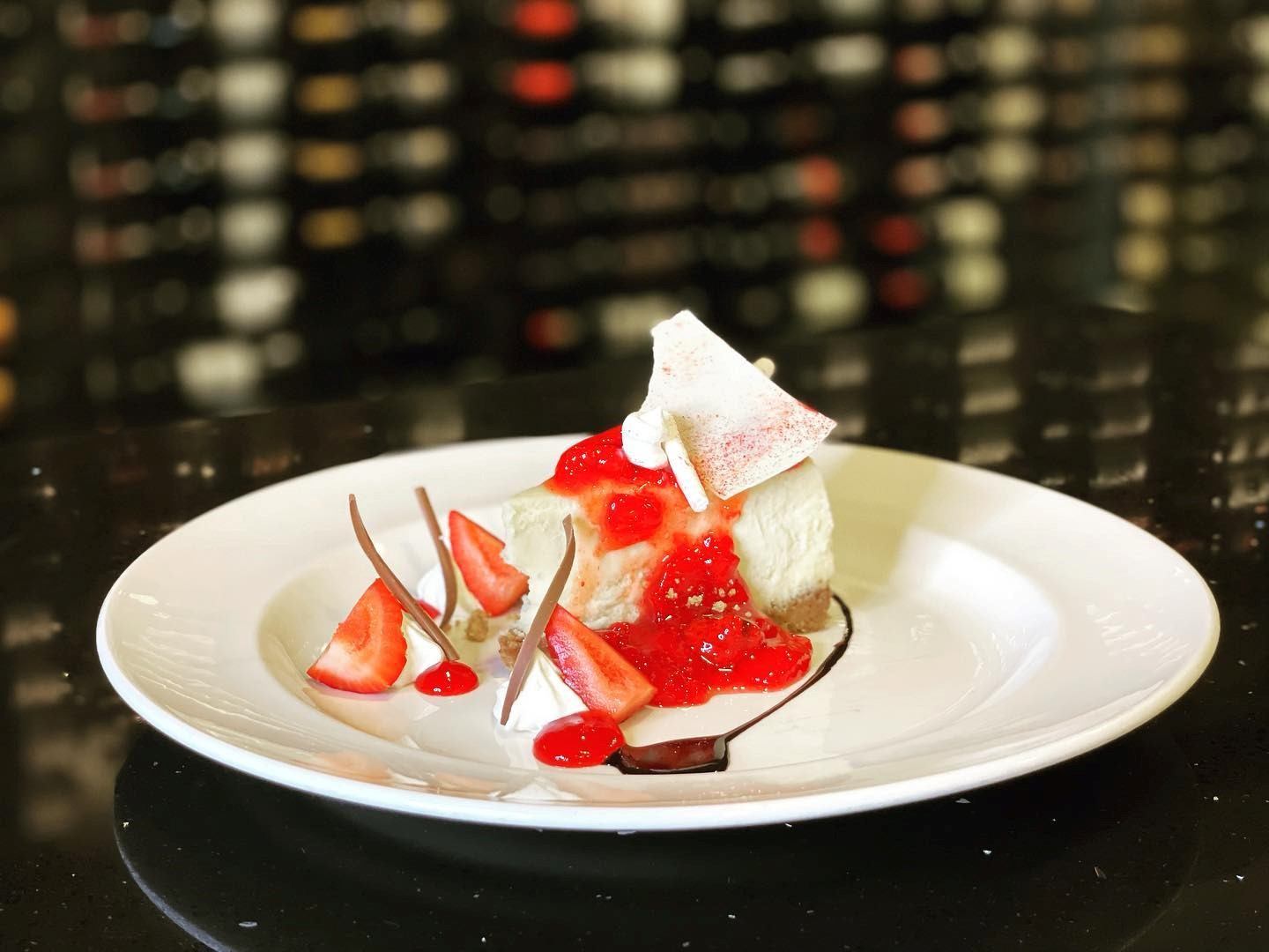 Plated dessert with cream, red fruit sauce, and chocolate drizzle on a white plate.