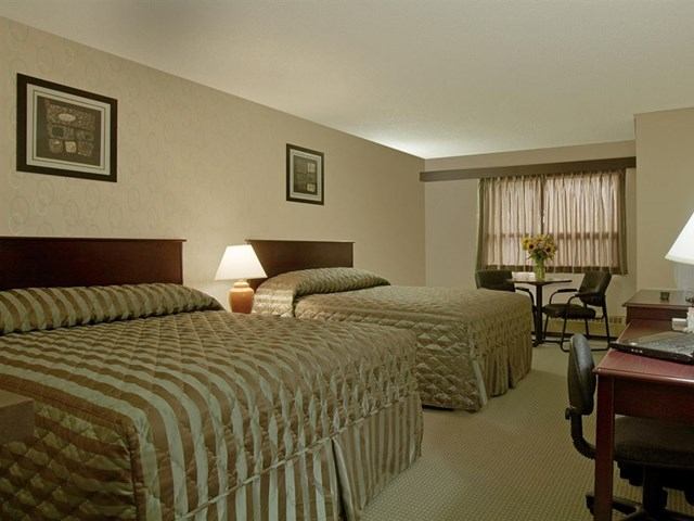 Hotel room with two double beds, desk, seating area, and warm lighting.