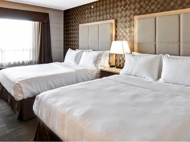 Hotel room at Canalta St. Paul with two beds, lamp, and window with curtains.