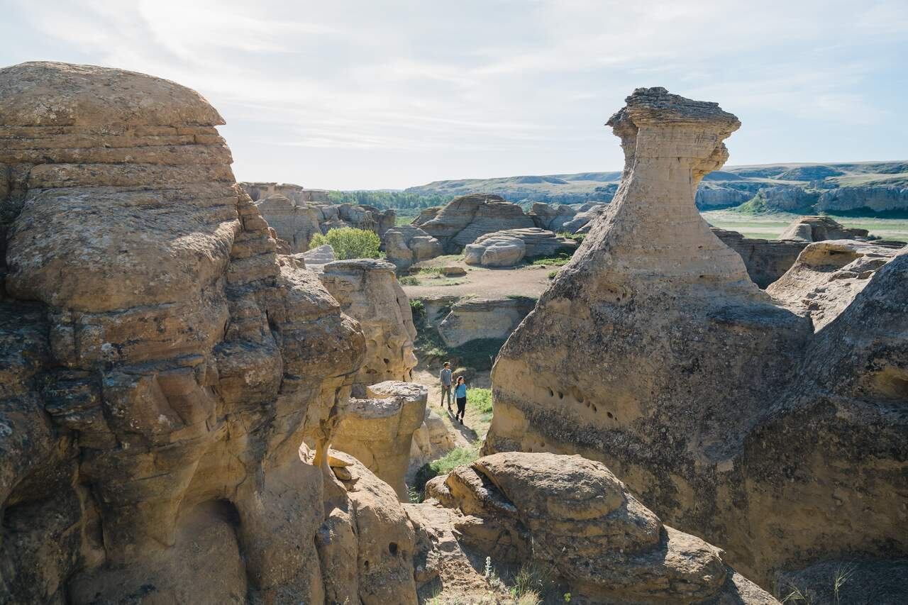 Sandstone hoodoos and cliffs surround two hikers walking along a narrow valley trail.