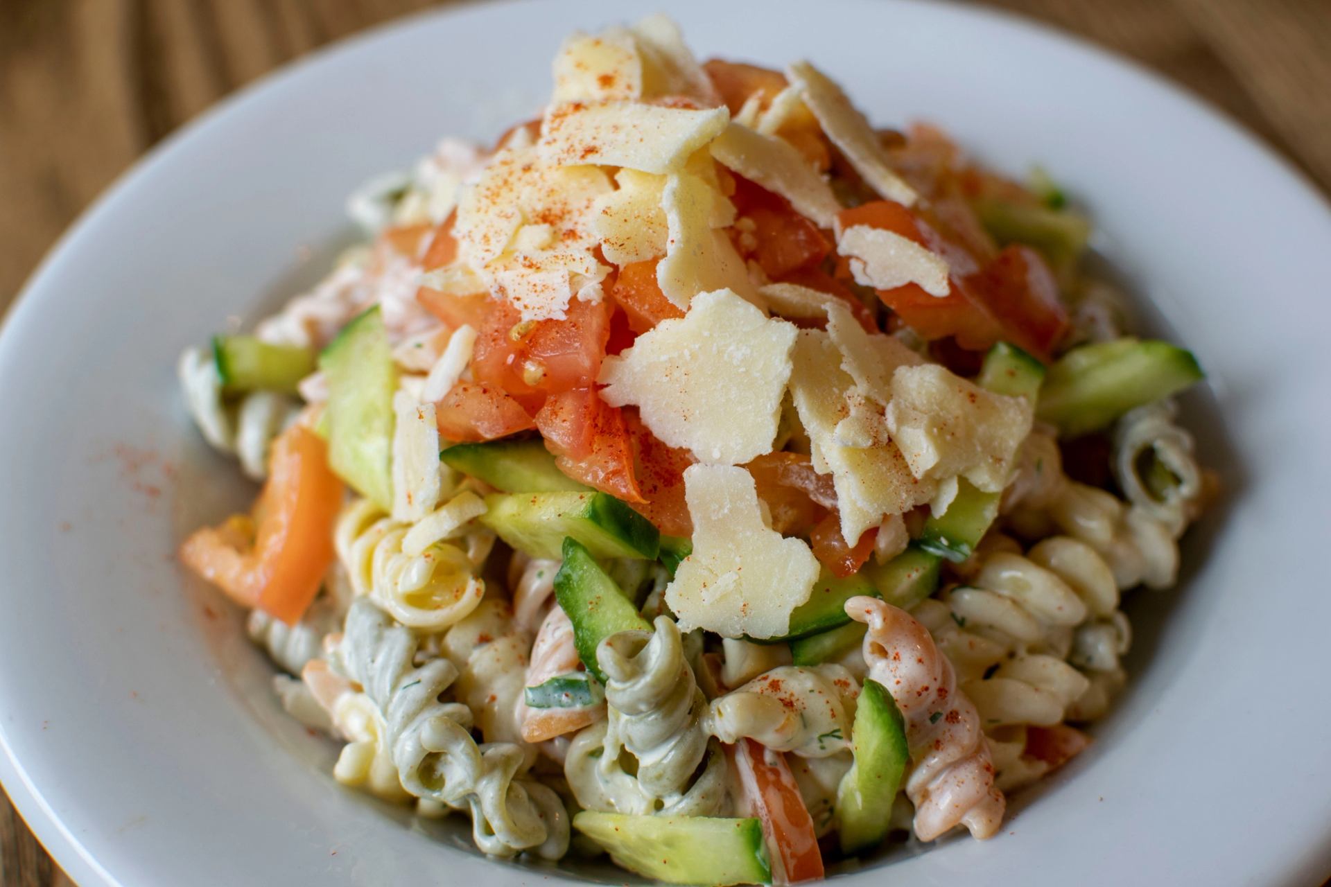 Spiral pasta salad with cucumbers, tomatoes, cheese slices, and spices.