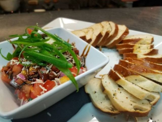 Appetizer with sliced bread and colorful veggie mix in a bowl, garnished with herbs.