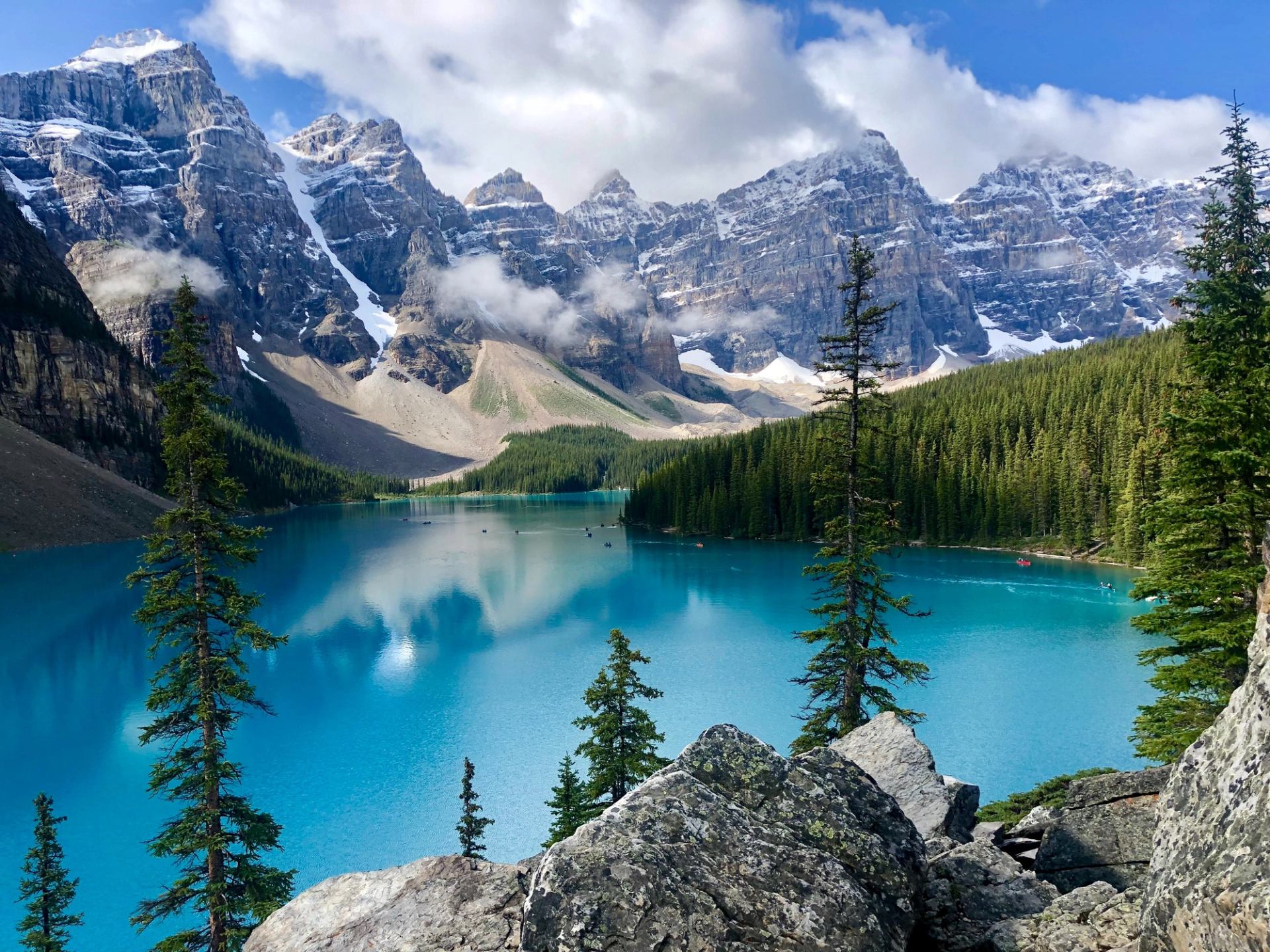 Turquoise Moraine Lake surrounded by pine trees and snowy Rocky Mountains under a blue sky.