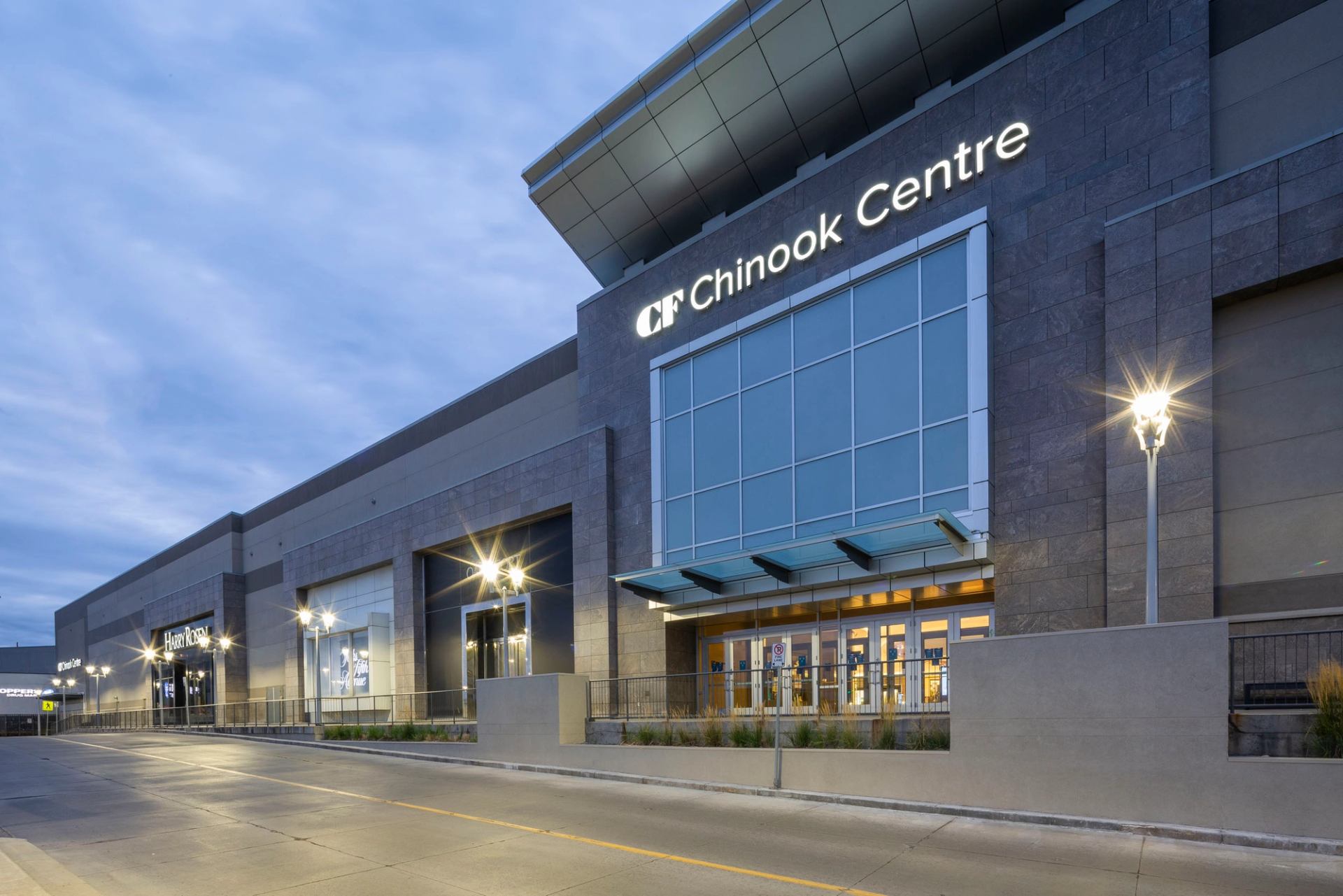 CF Chinook Centre exterior with lit sign, glass entrance and streetlights.