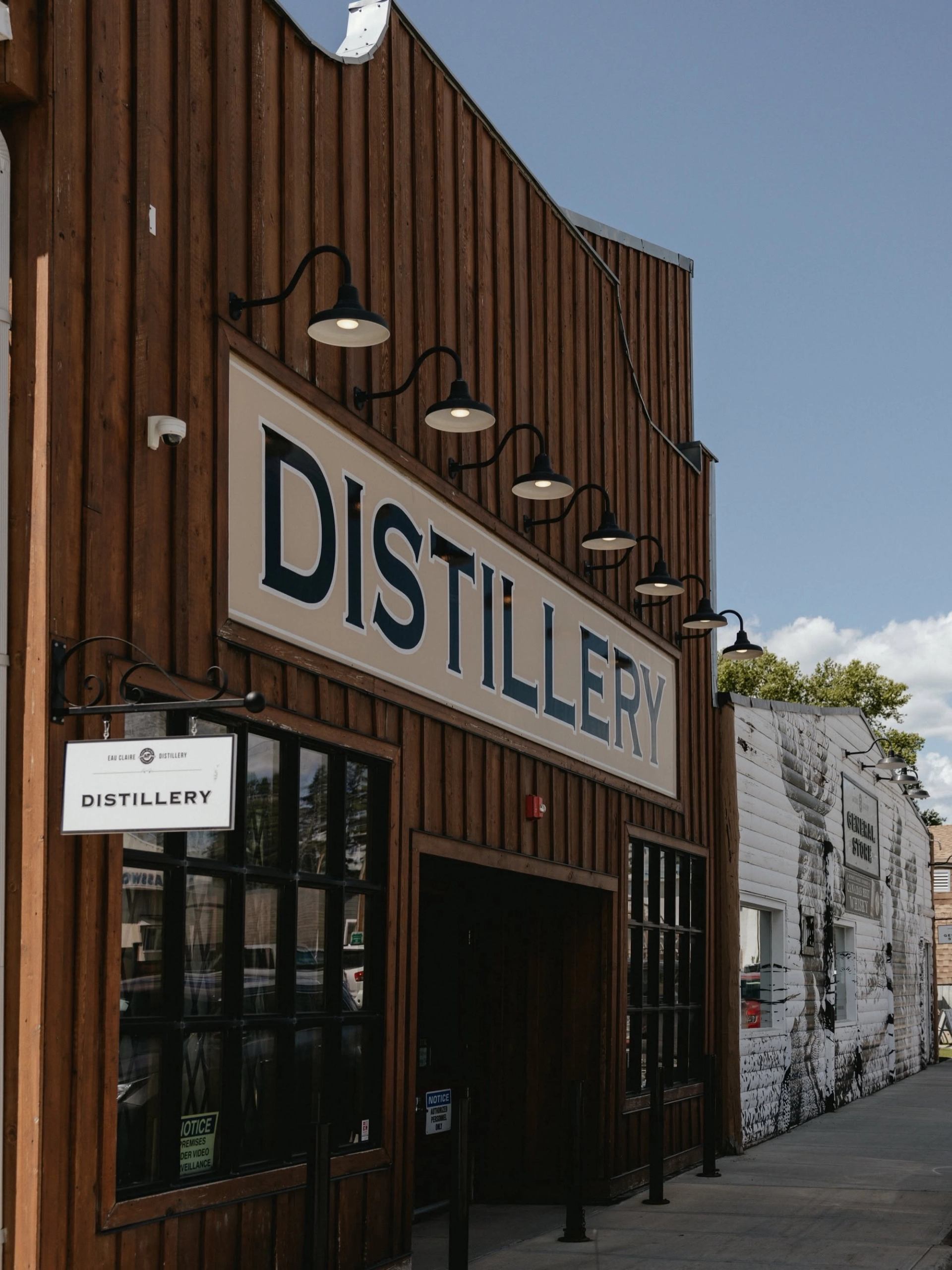 A historic wooden building with a large distillery sign lines a small-town street under a clear sky.