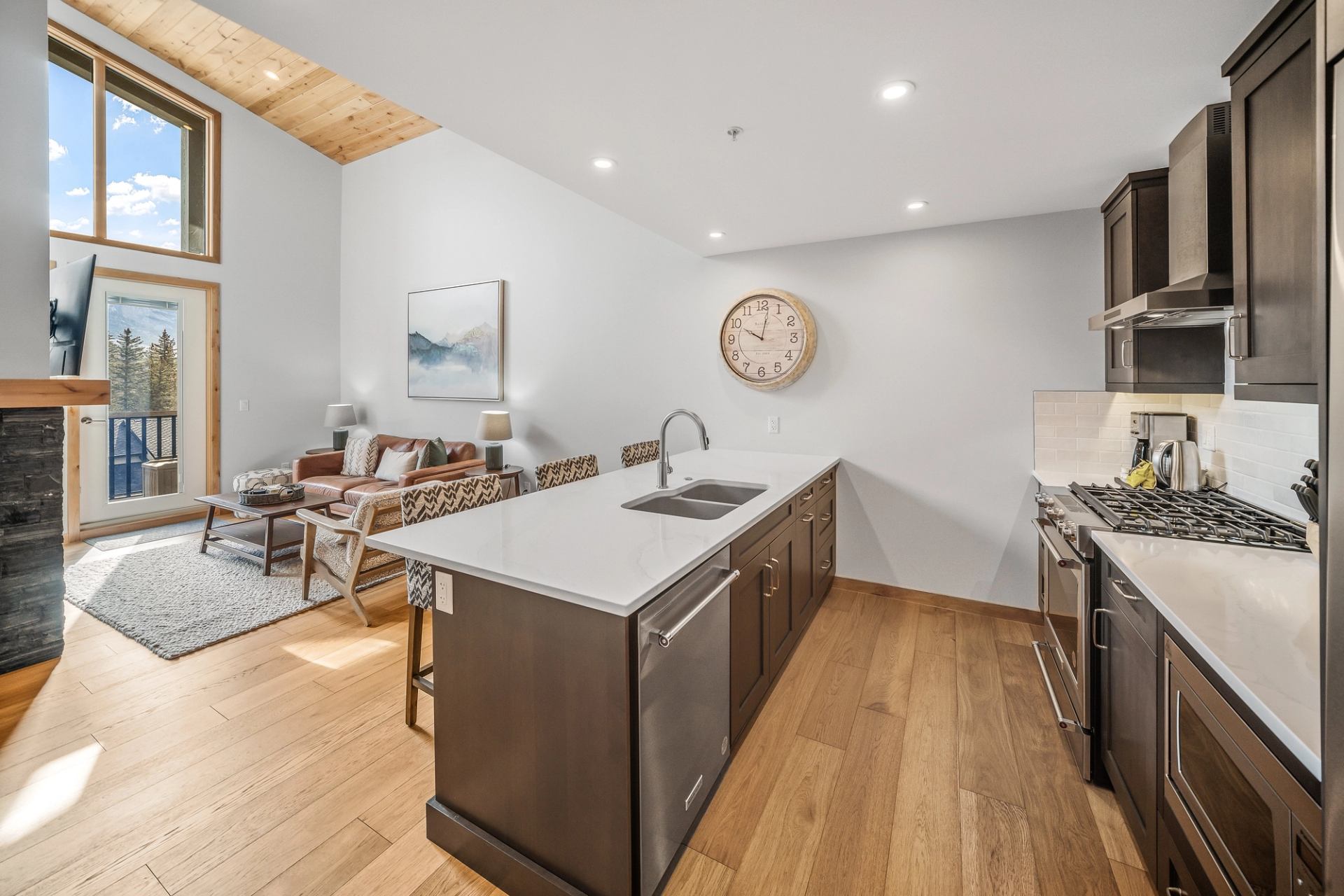 Open-concept kitchen and living room with island, gas stove, sofa and balcony view.