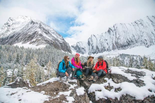 Group of friends sitting on a snowy rock with views of the mountains in Spray Valley Provincial Park.