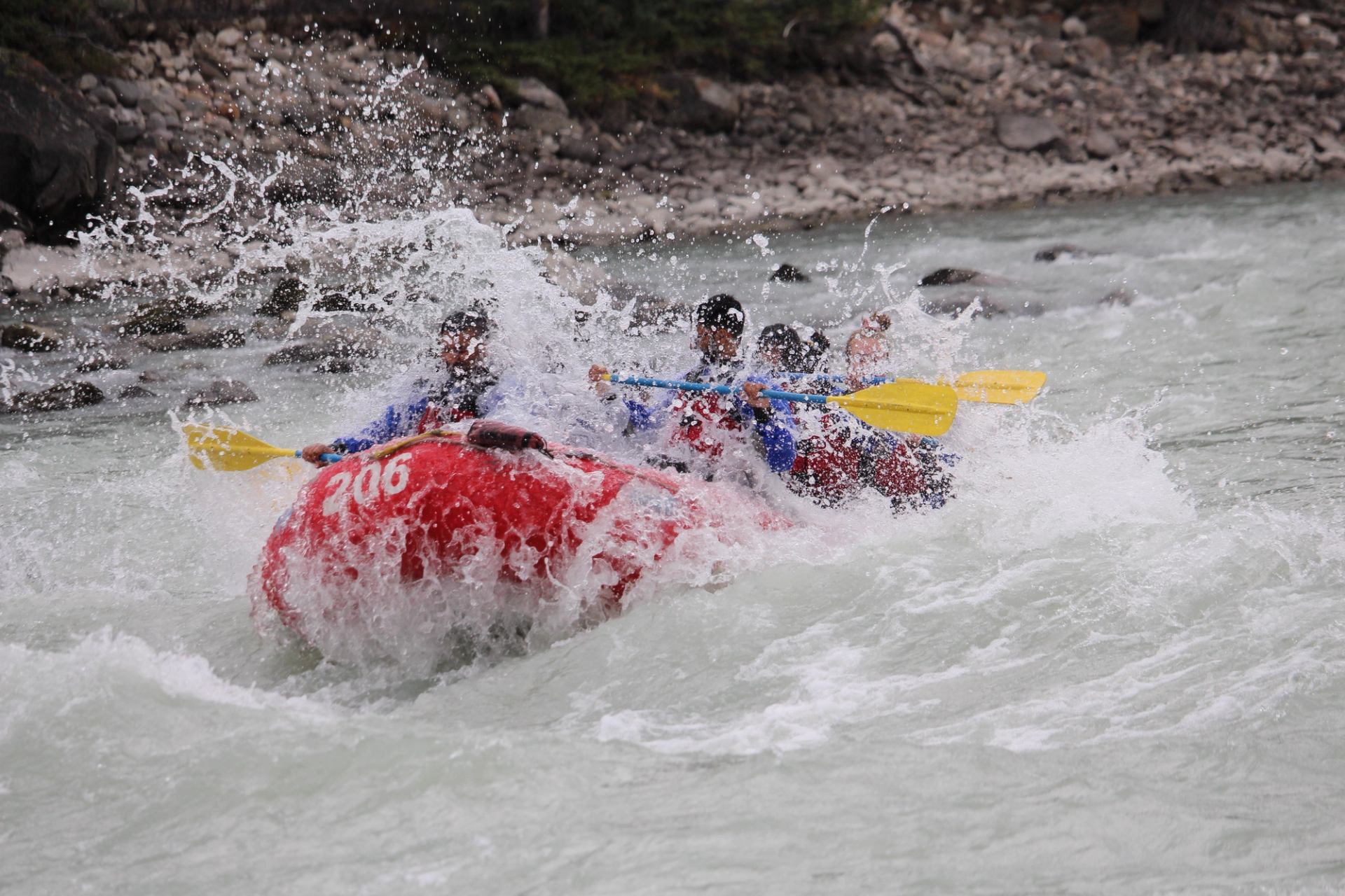 Rafting kayaks with paddlers in whitewater rapids on a river, splashing into foam.