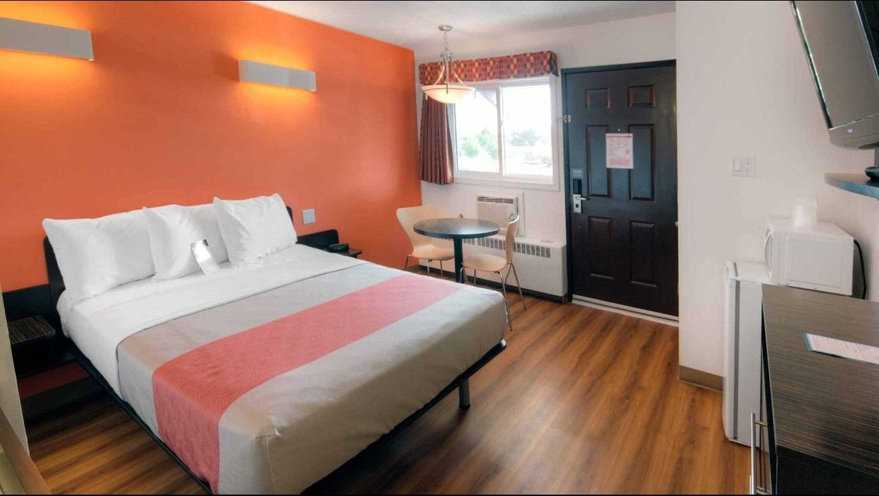 Motel room with double bed, small table and chair, kitchenette counter, and dark front door.