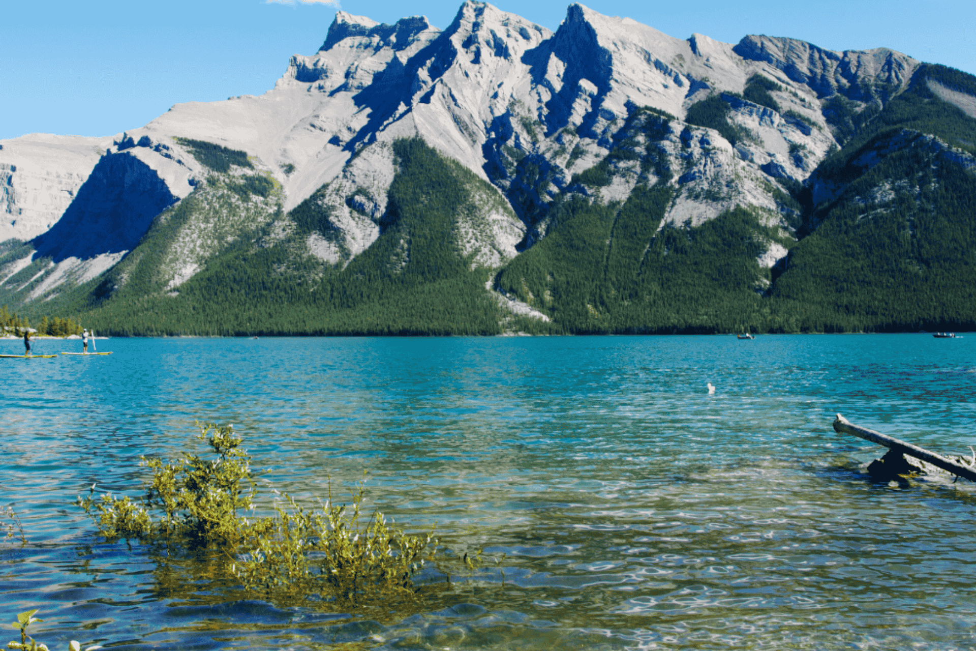 Clear turquoise lake with rocky mountains rising behind it on a bright sunny day.