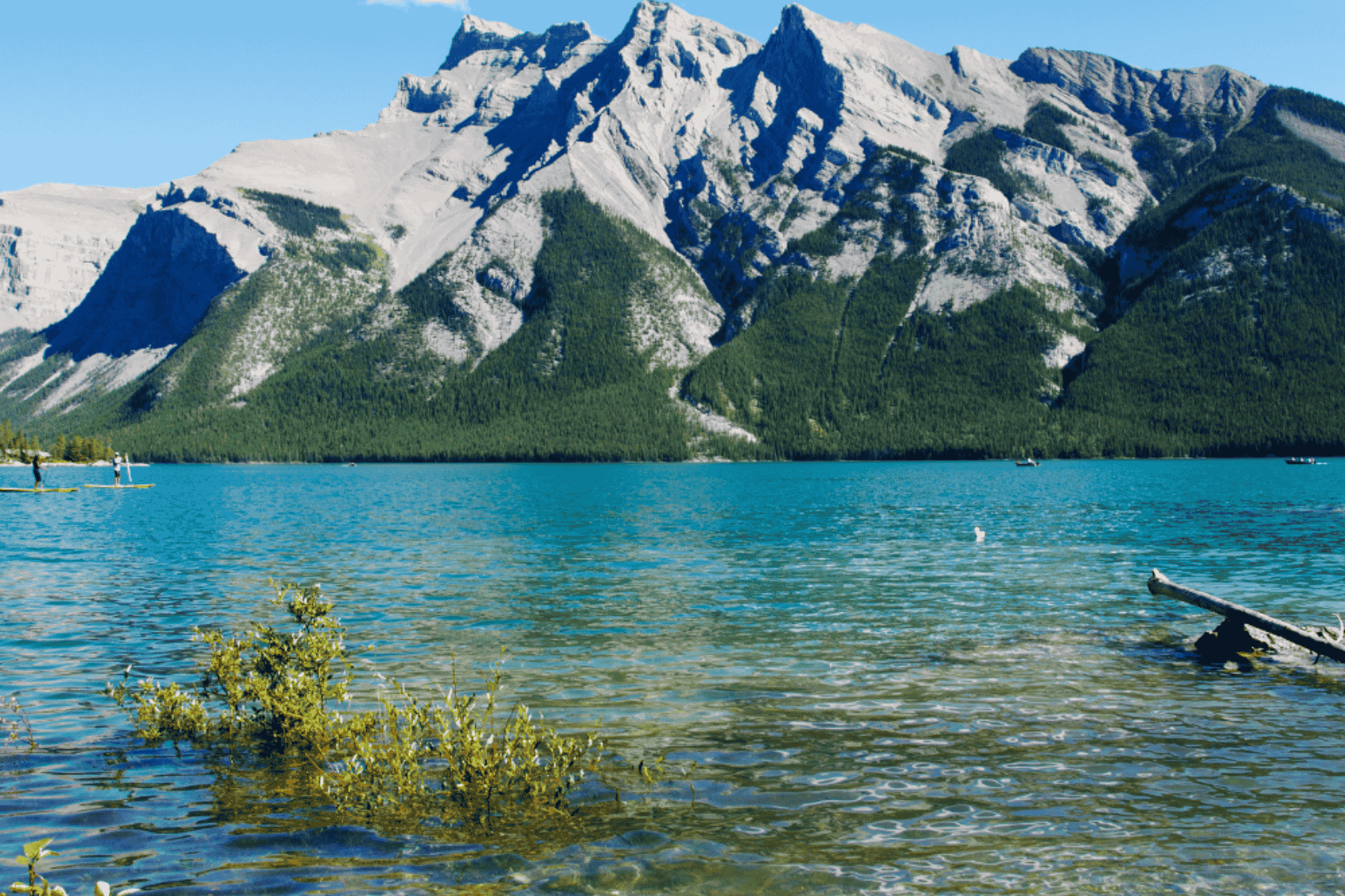 Clear turquoise lake with rocky mountains rising behind it on a sunny day.