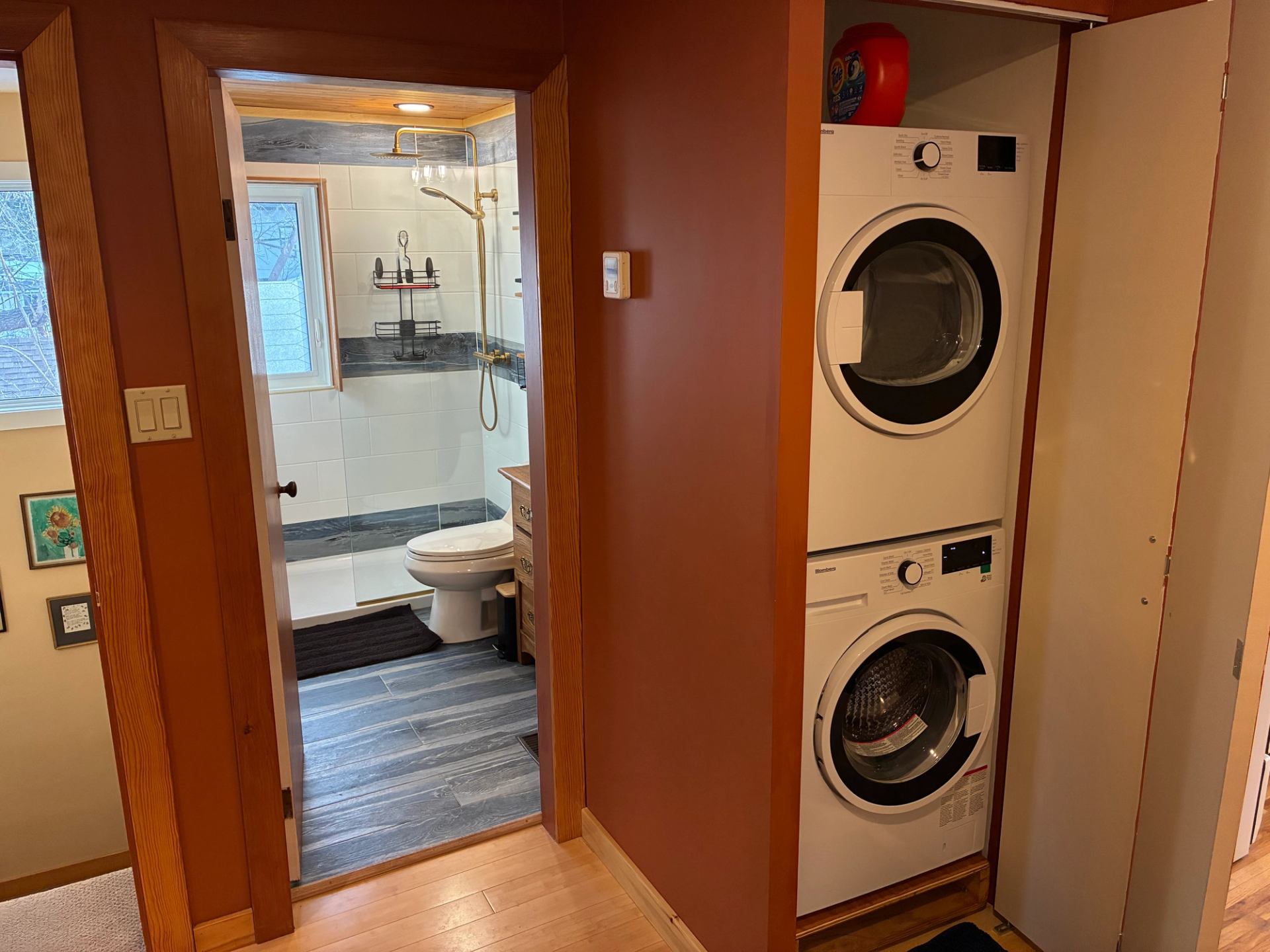 Hallway with open bathroom door beside closet housing stacked washer and dryer.