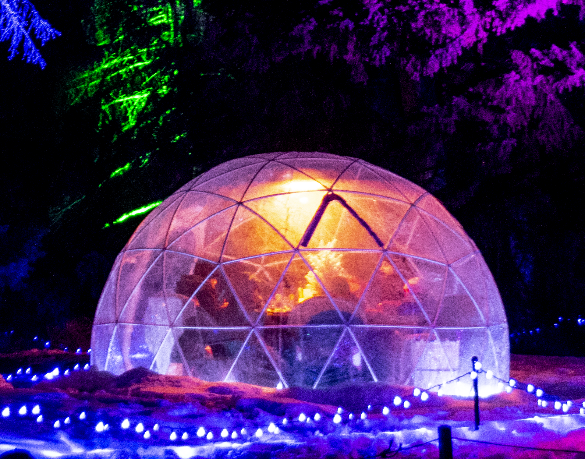 Illuminated dome structure glowing with vibrant purple and orange lights in a snowy setting.