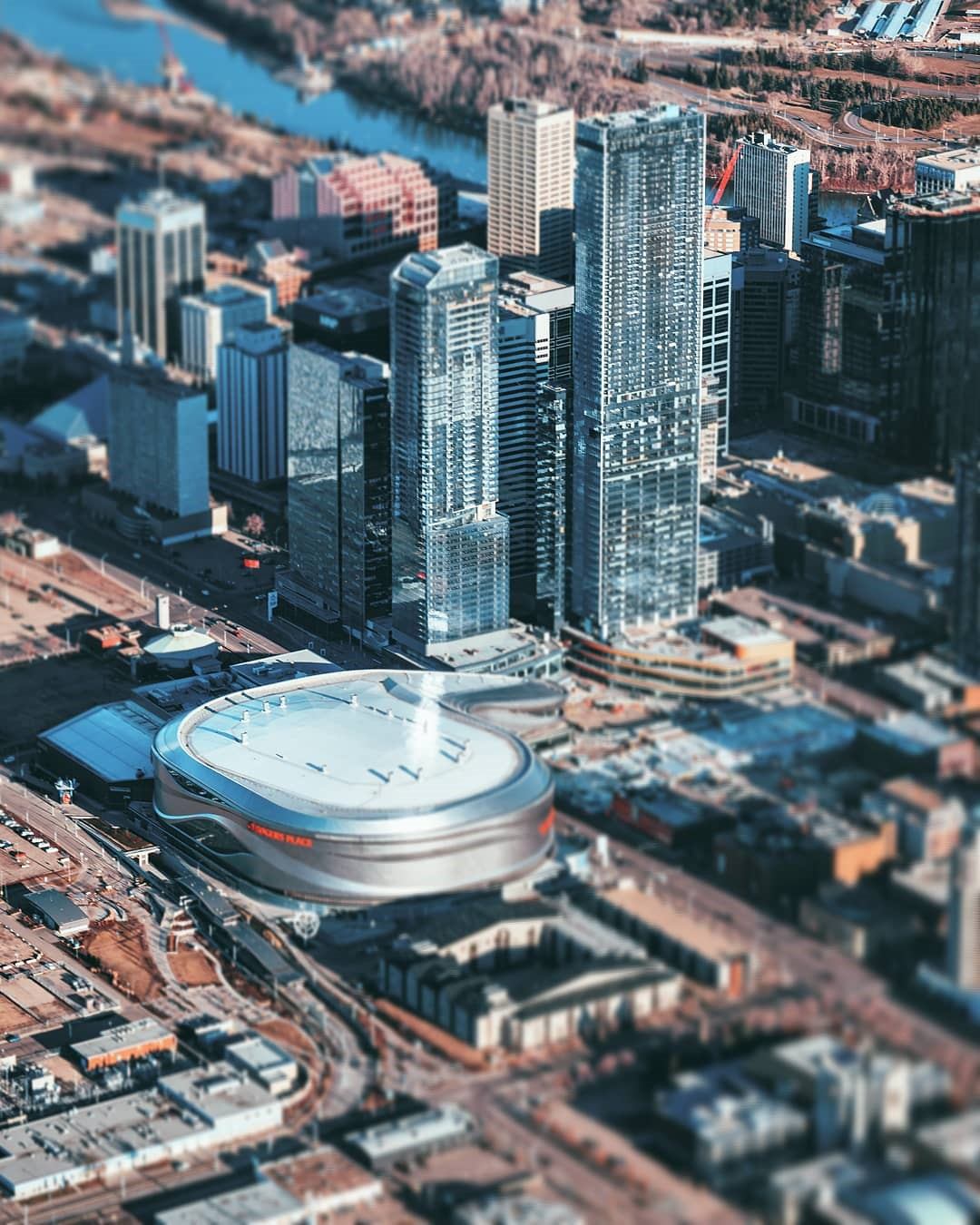 Aerial view of Rogers Place arena and downtown high-rise towers near river.