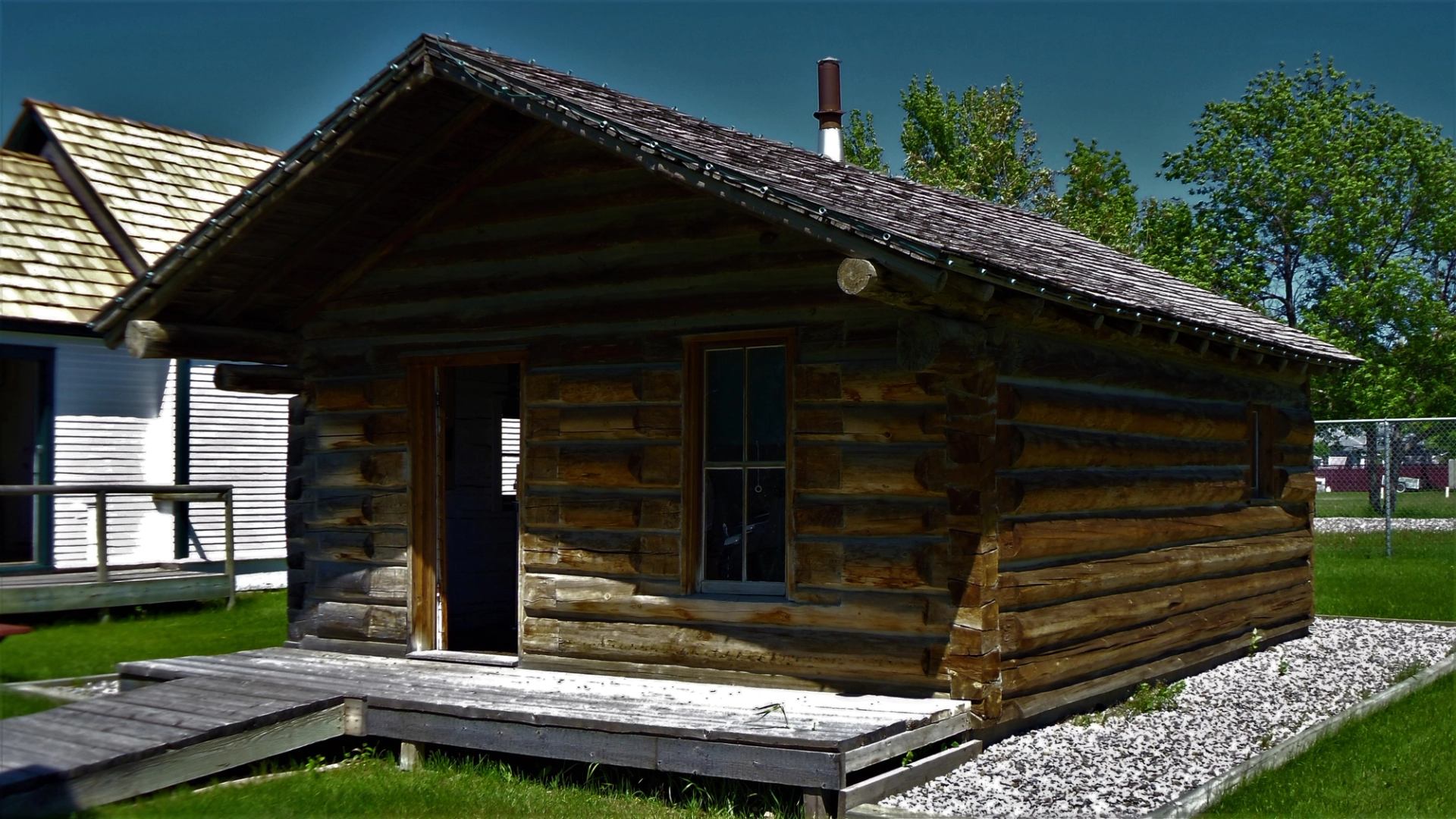 Small log cabin with wooden ramp, surrounded by green grass and trees.