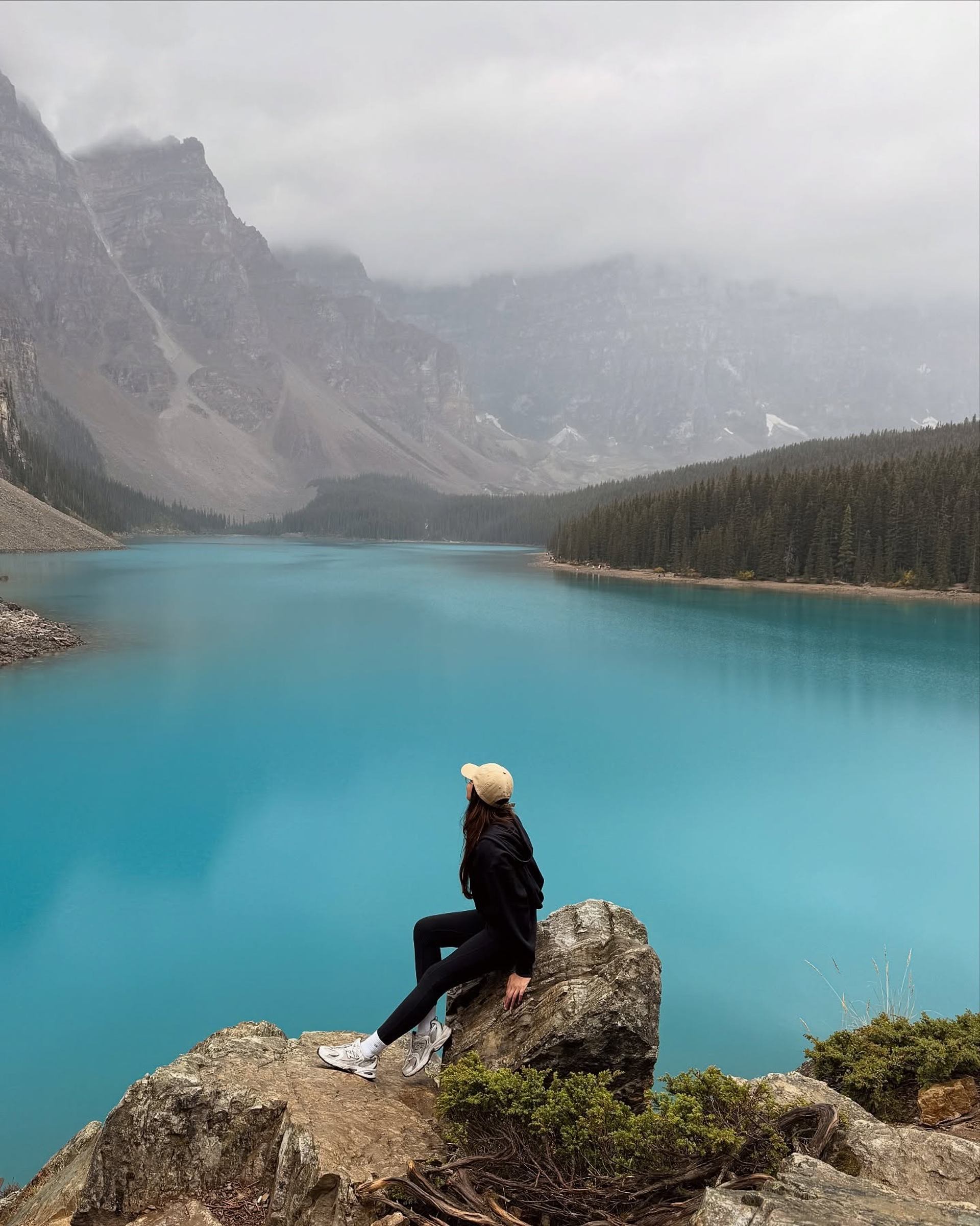 Person sitting on a rock overlooking a turquoise lake surrounded by mountains.