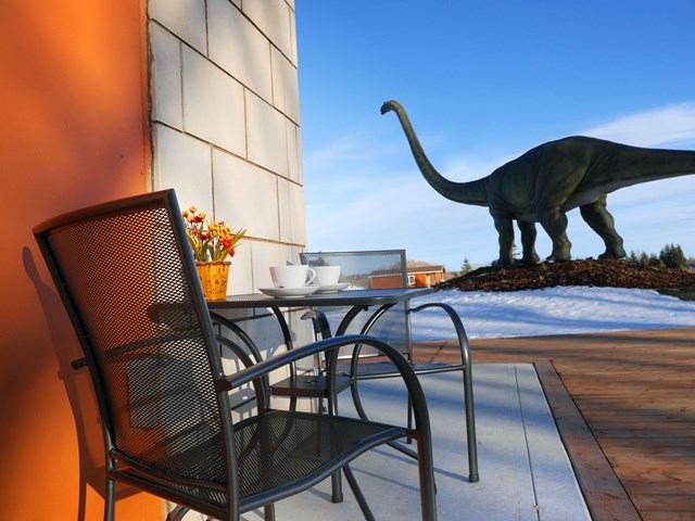 Patio table with cups beside orange wall, dinosaur statue beyond snow.