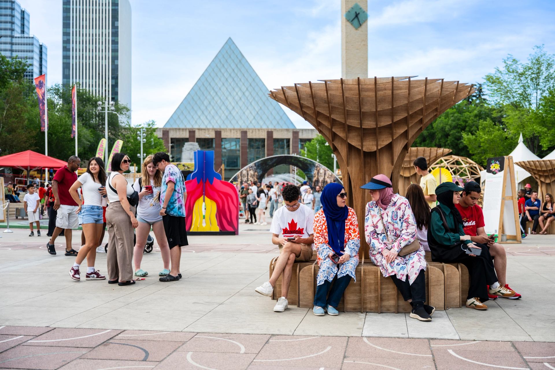 Crowd gathers around wooden seating sculpture in urban square with modern buildings.