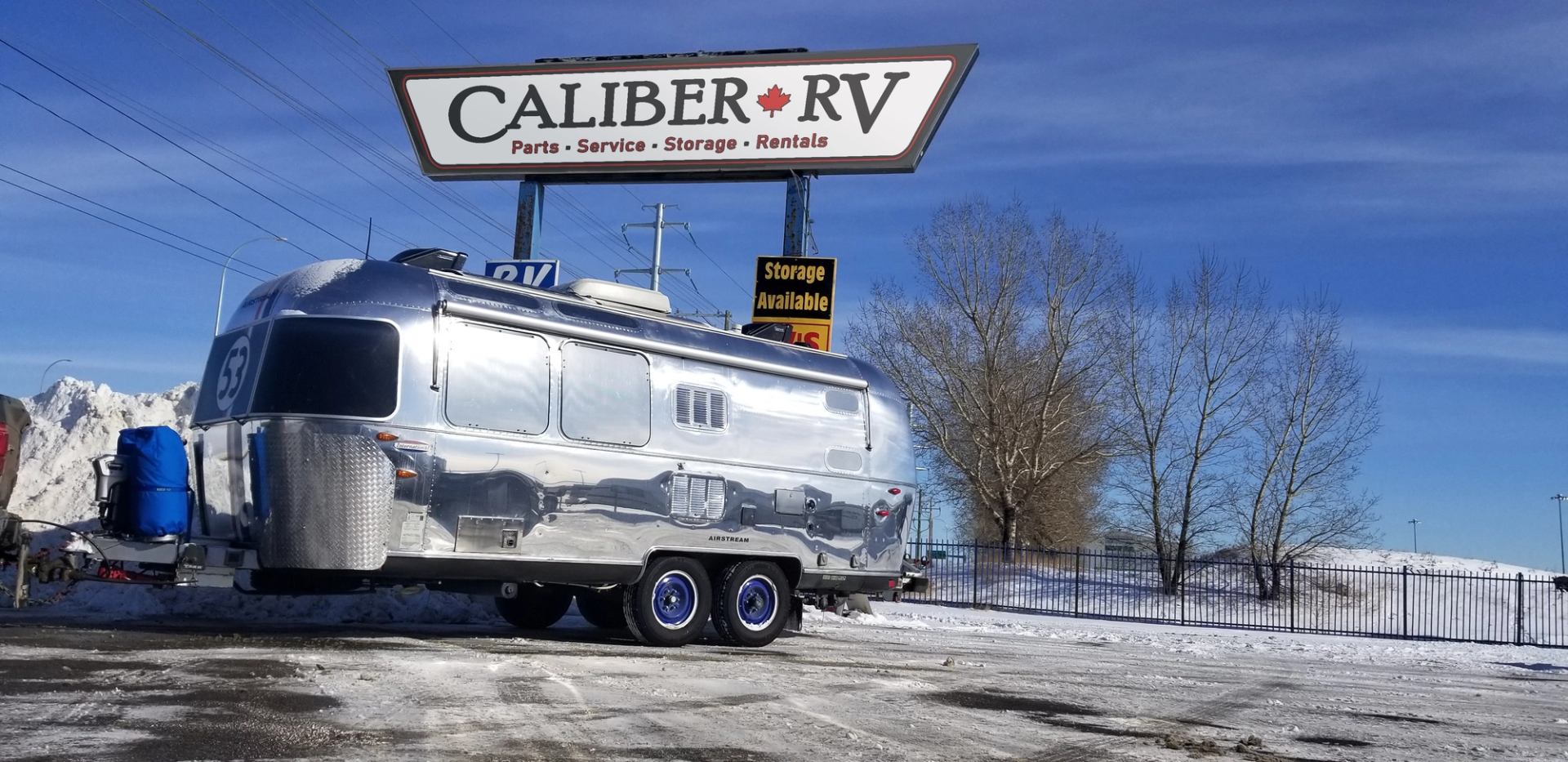 Silver RV parked in front of Caliber RV sign on a sunny day.