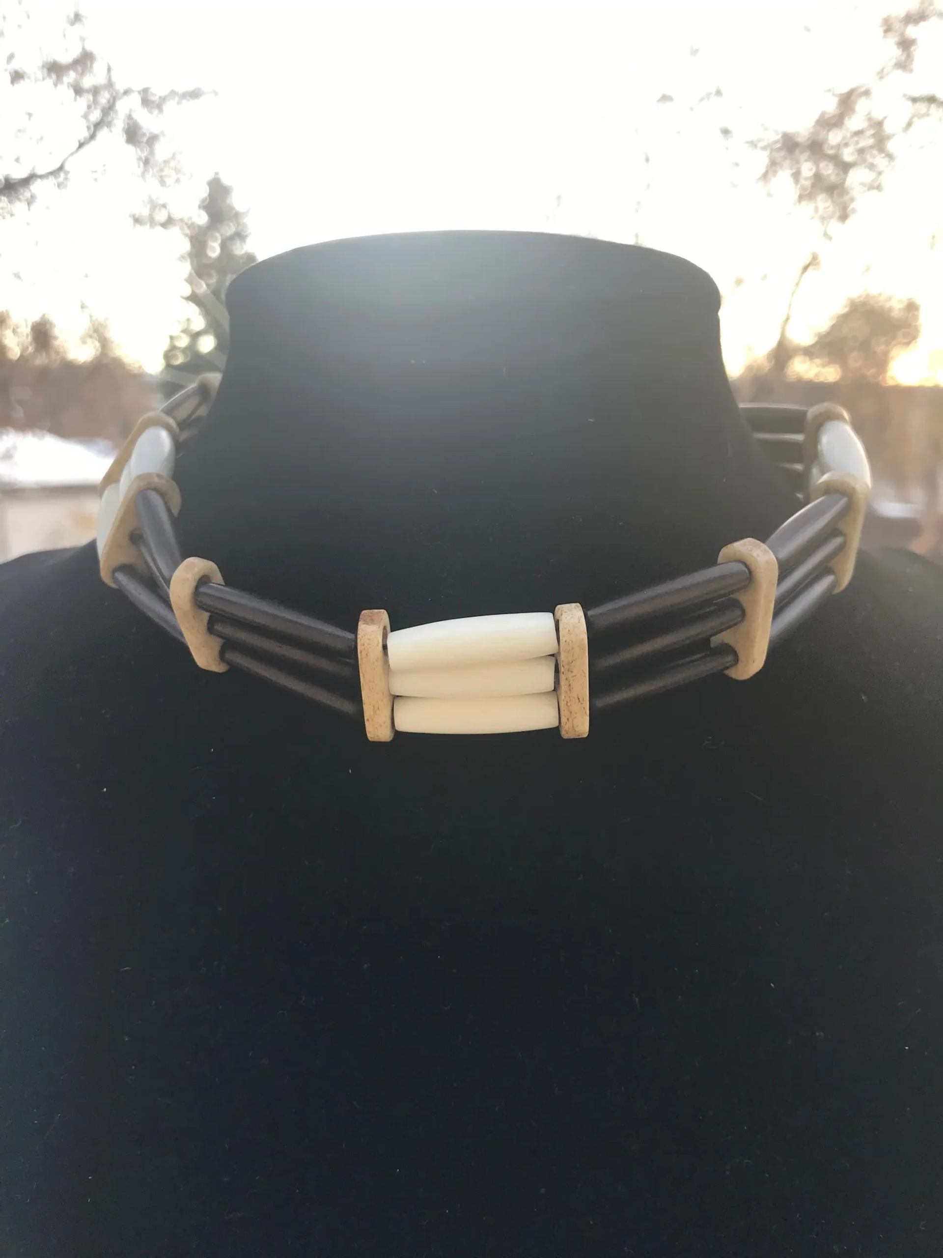 Black and white beaded choker necklace displayed on a black velvet bust outdoors.