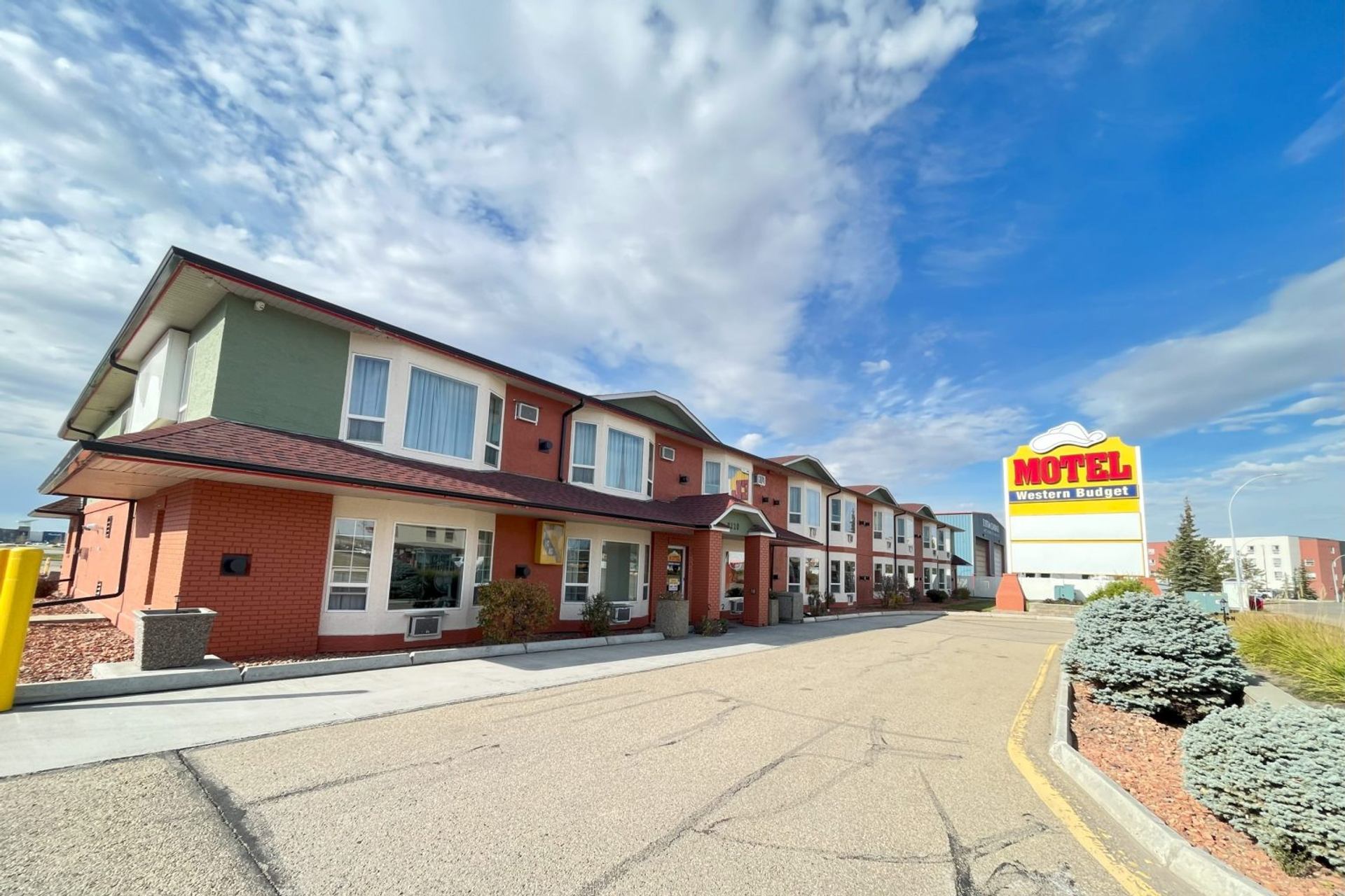 Western Budget Motel with red roof and large roadside sign under clear blue sky.