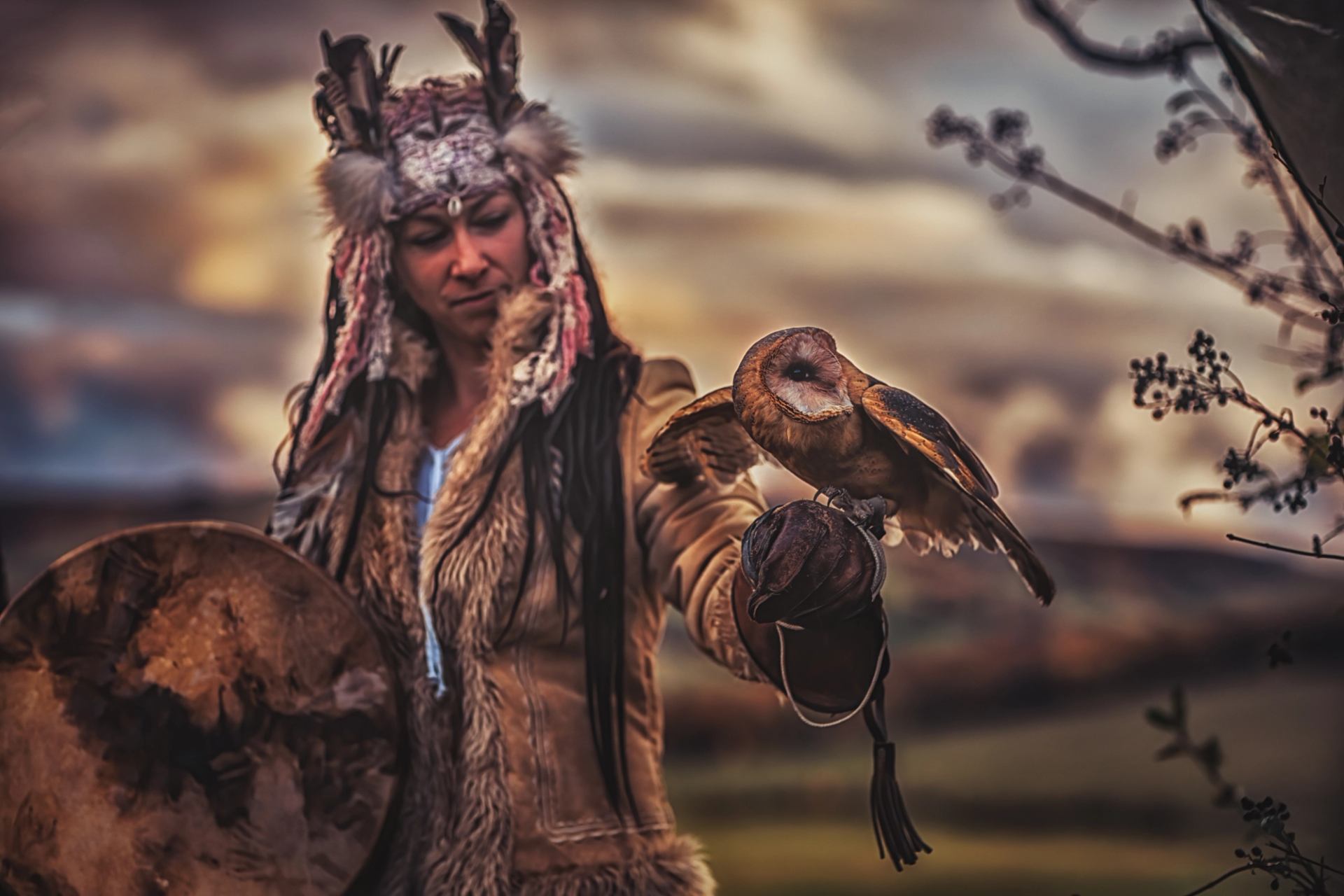 Person in fur-trimmed coat holds a barn owl on gloved hand outdoors.