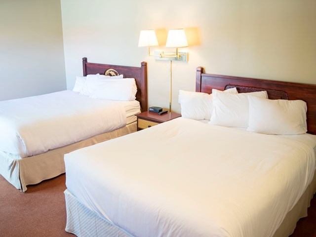 Hotel room with two double beds, white linens, and wall-mounted lamps.