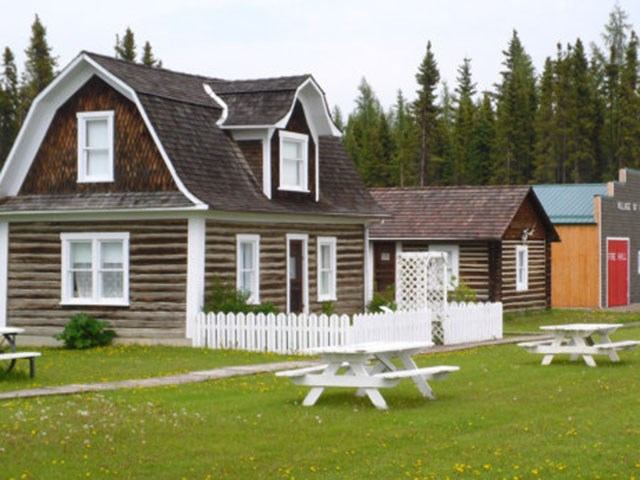 Historic wooden buildings with picnic tables in a green, forested village setting.