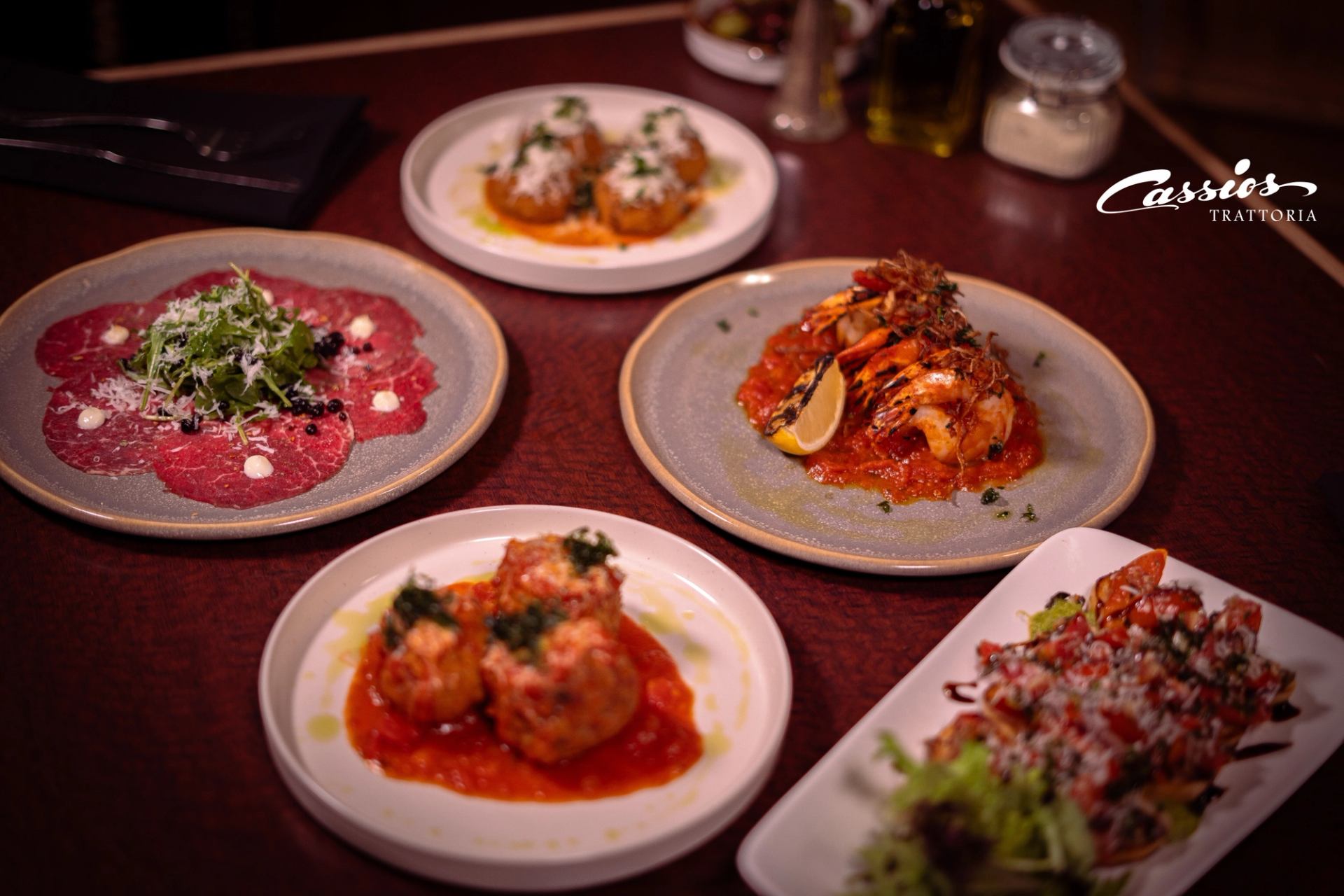 Italian dishes on restaurant table, including carpaccio, prawns in sauce and arancini.