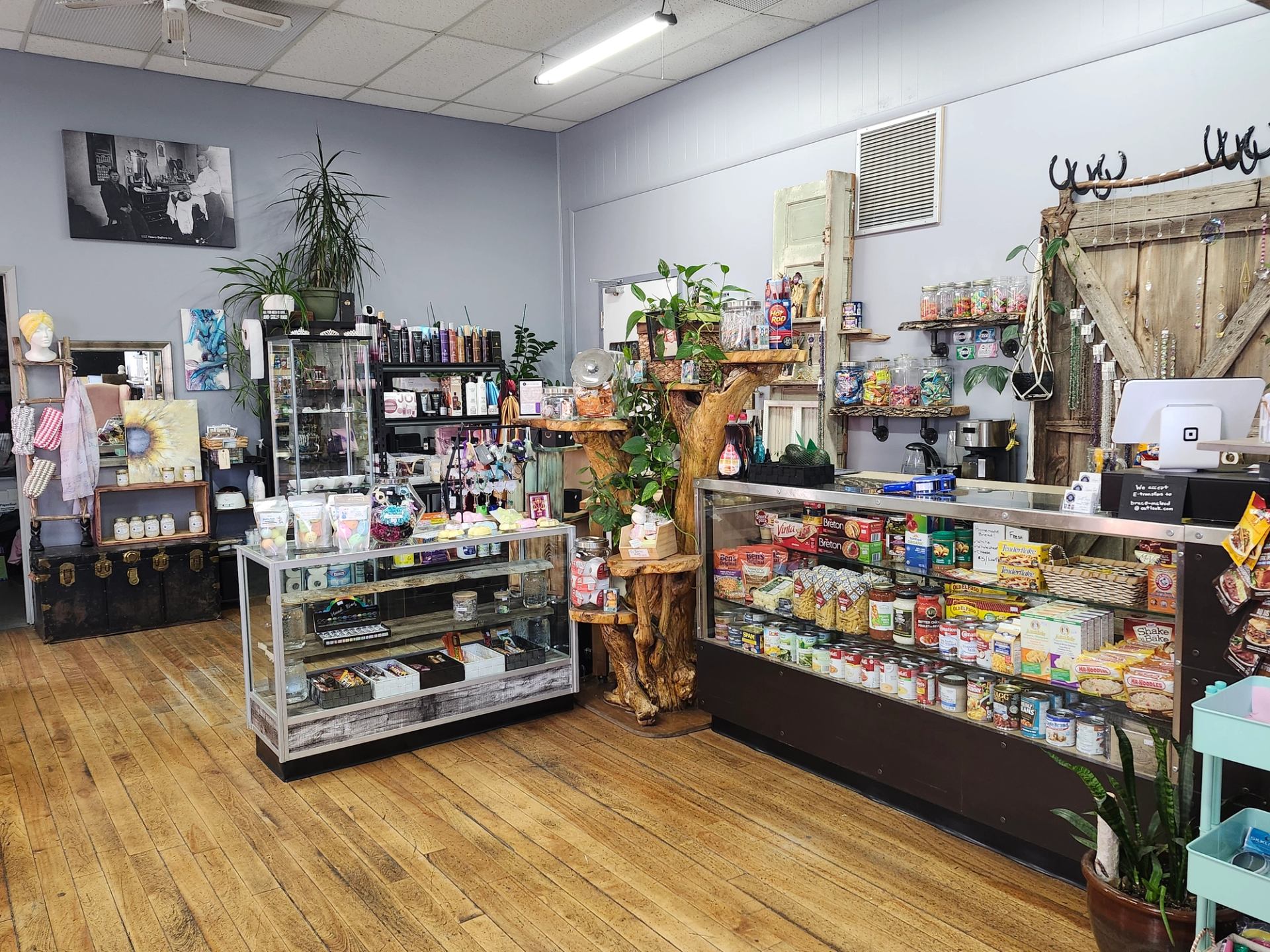 Interior of an eclectic general store with wooden floors, shelves of varied products, and a grocery display case.