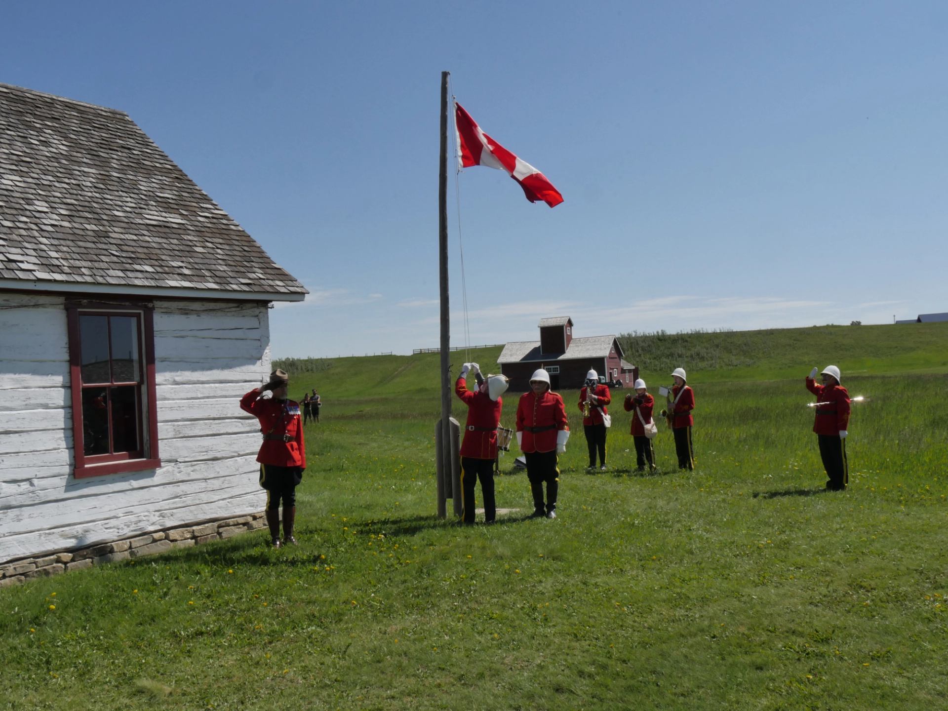 A Canada flag is raised during a ceremonial gathering on open grassland at Bar U Ranch.