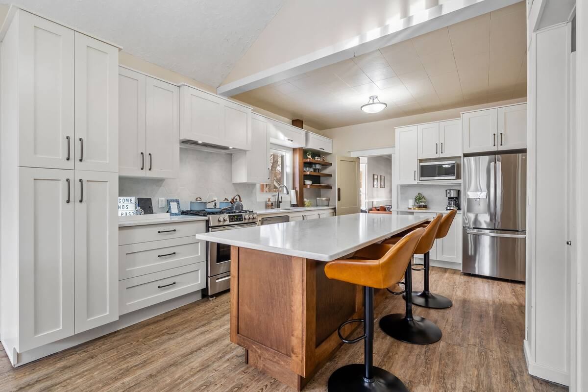 An open kitchen with a bar and barstools - a gas range and fridge